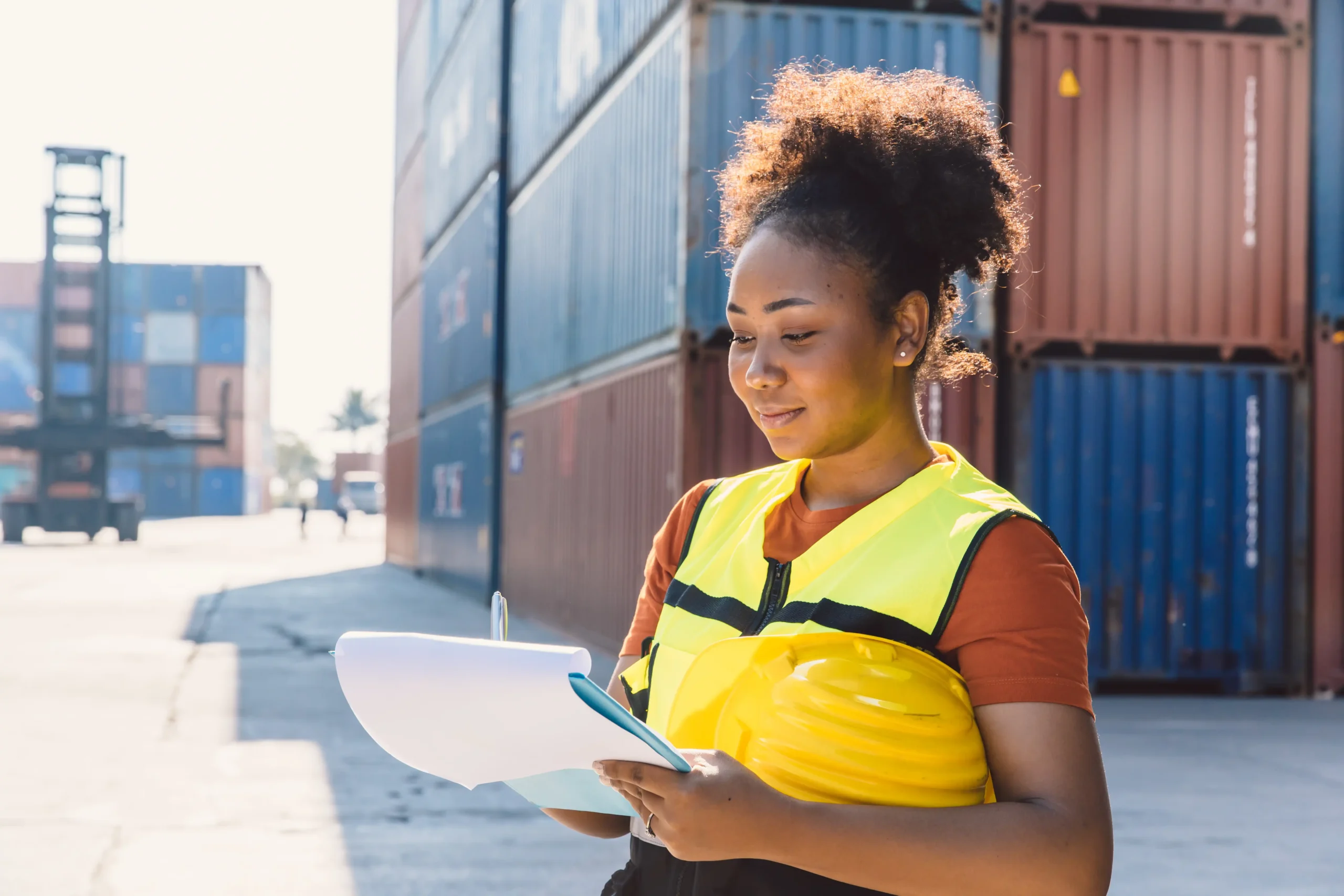 Customs officer checking import/export documentation in a shipping yard with stacked cargo containers.