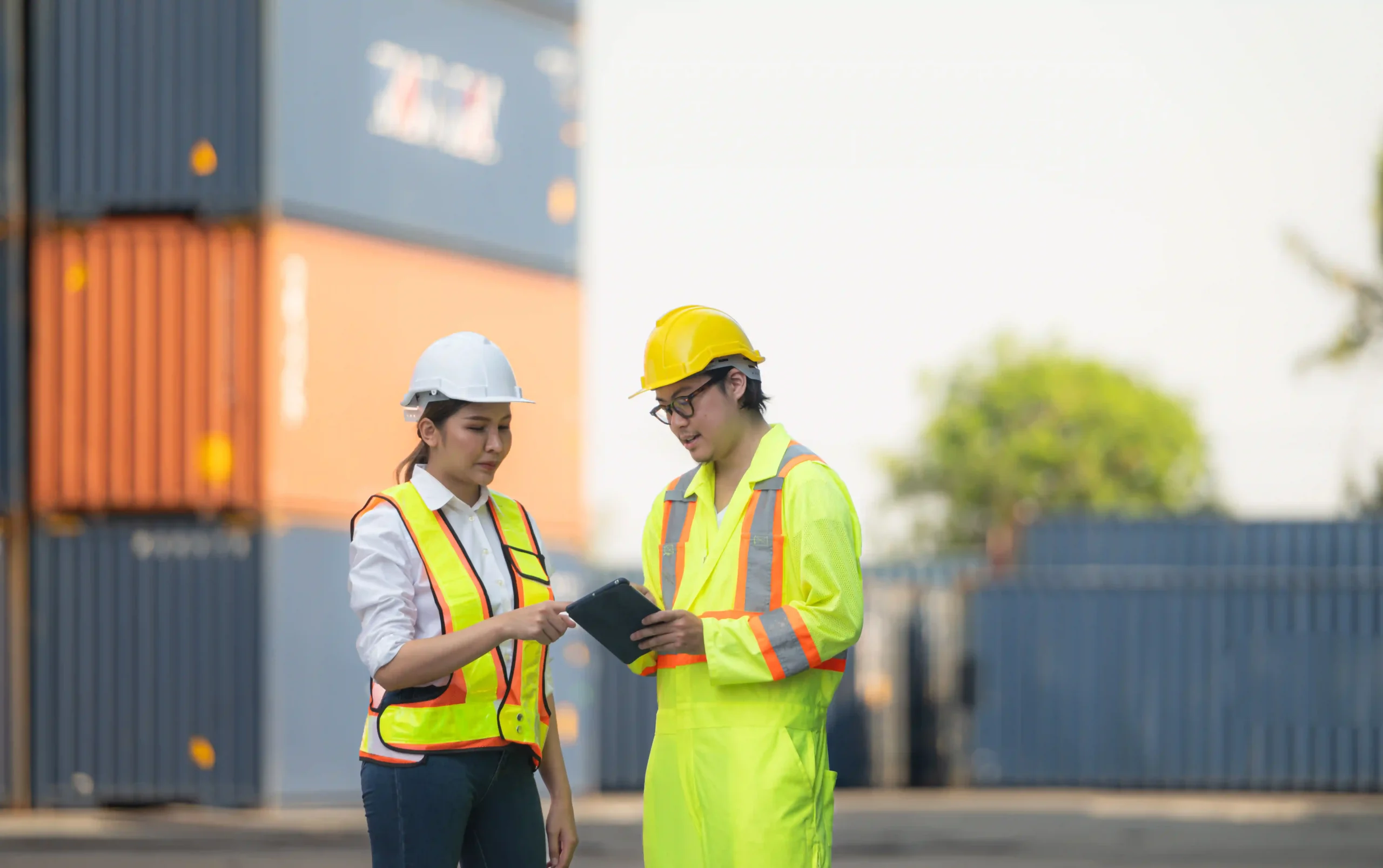 Logistics professionals reviewing order fulfillment data on a tablet at a shipping container yard.