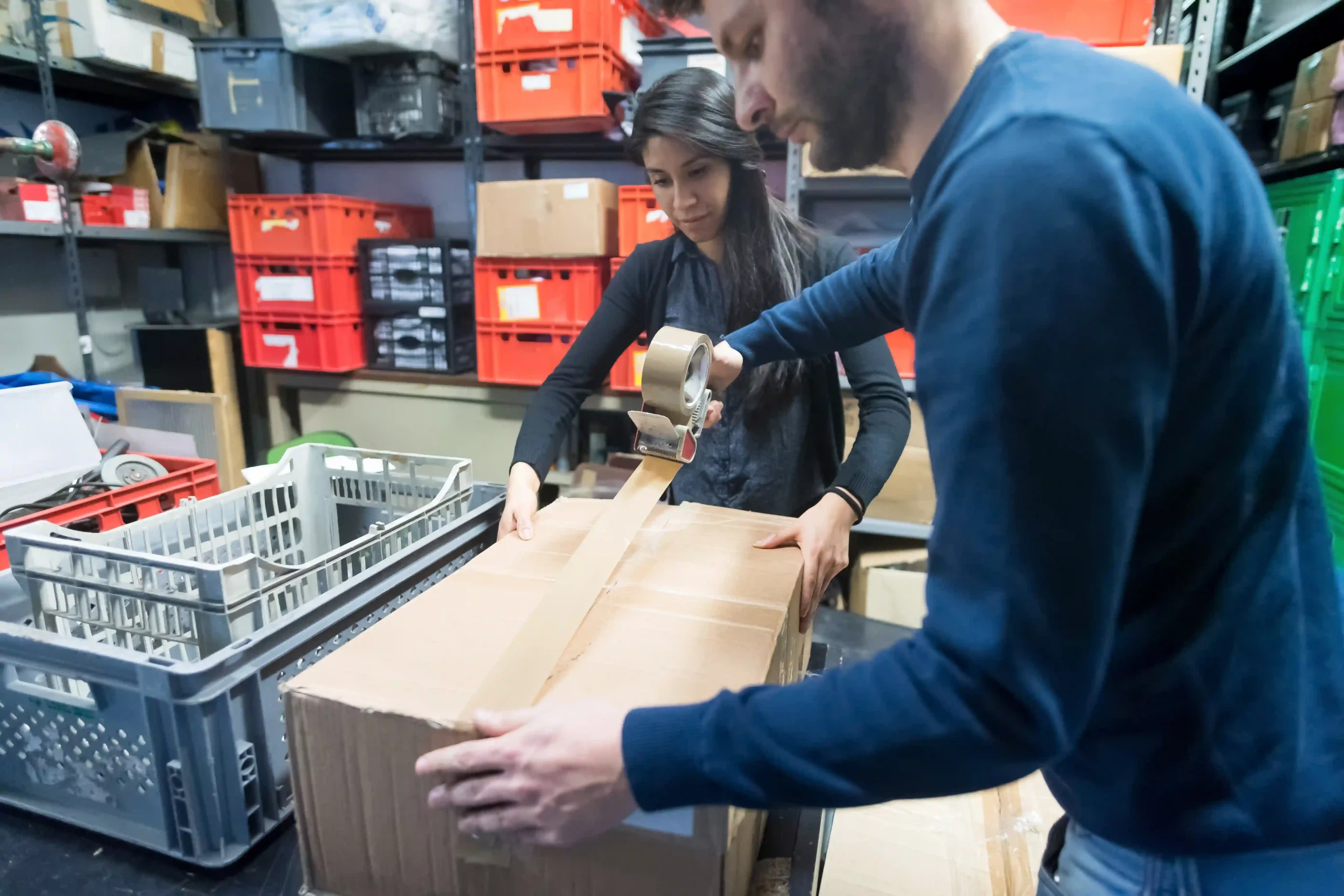 Two warehouse workers sealing a package as part of the pick and pack travel process, ensuring efficient order fulfillment.