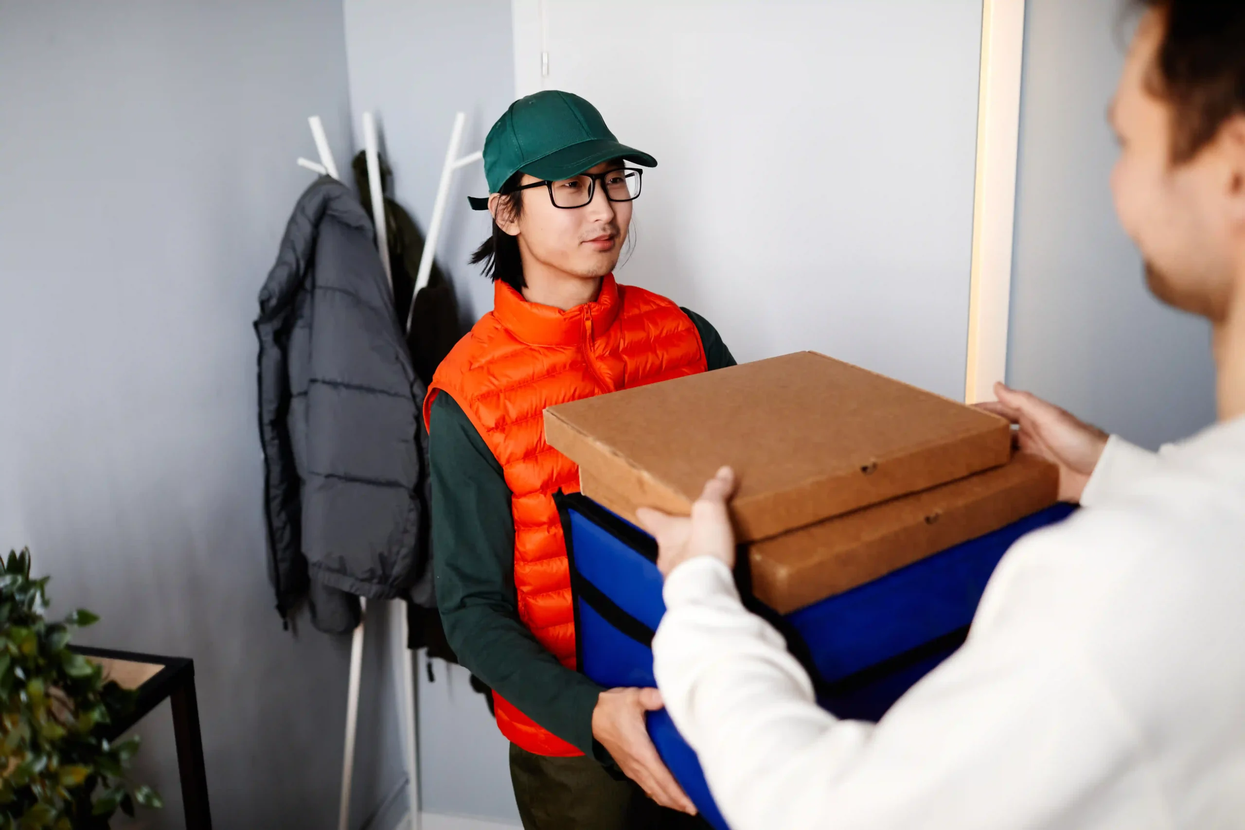 A last-mile delivery courier handing over pizza boxes to a customer at their doorstep.