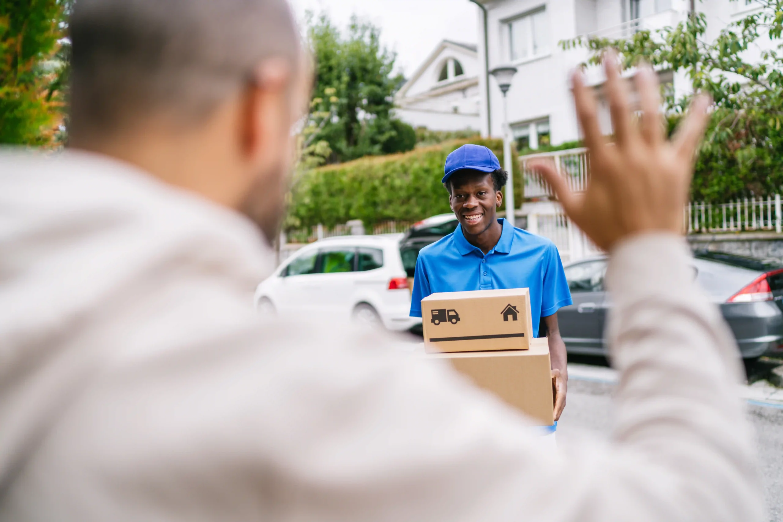 A happy customer waves as a last-mile delivery worker hands over a package at their home.