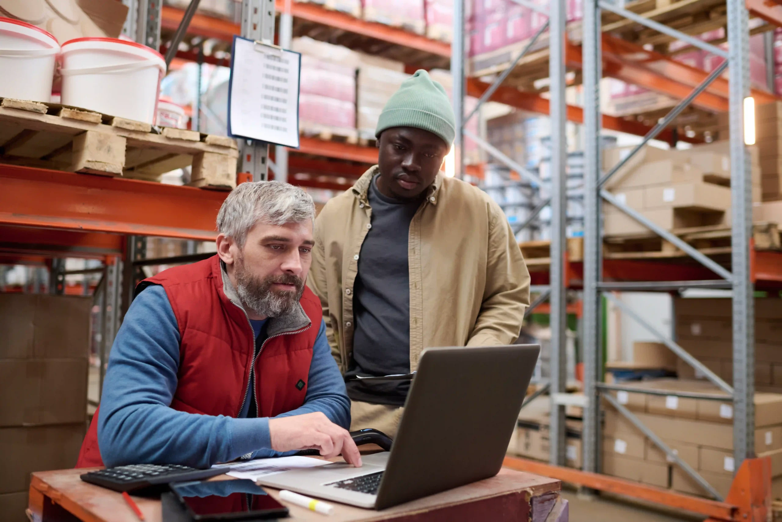 Warehouse manager and team member reviewing transportation logistics on a laptop in a warehouse setting.