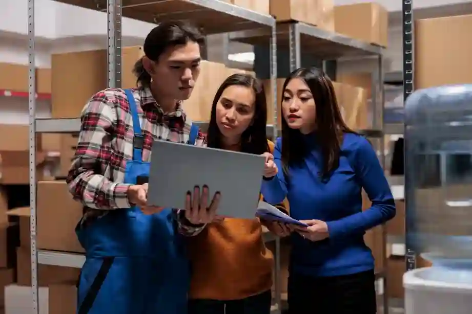 Warehouse employees analyzing orders and inventory using a laptop in a postal facility.