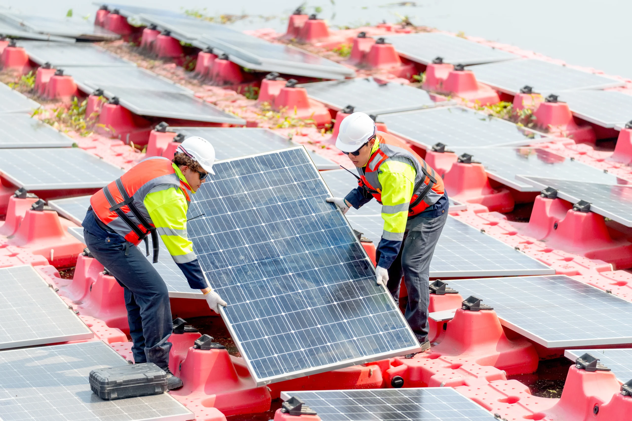 Workers carrying a solar panel during a renewable energy installation on a floating platform.