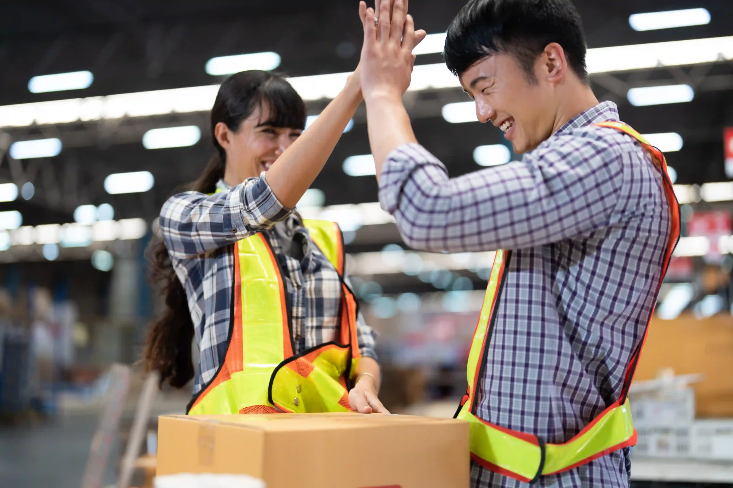 Two warehouse workers celebrating successful storage organization while working on small warehouse storage solutions.