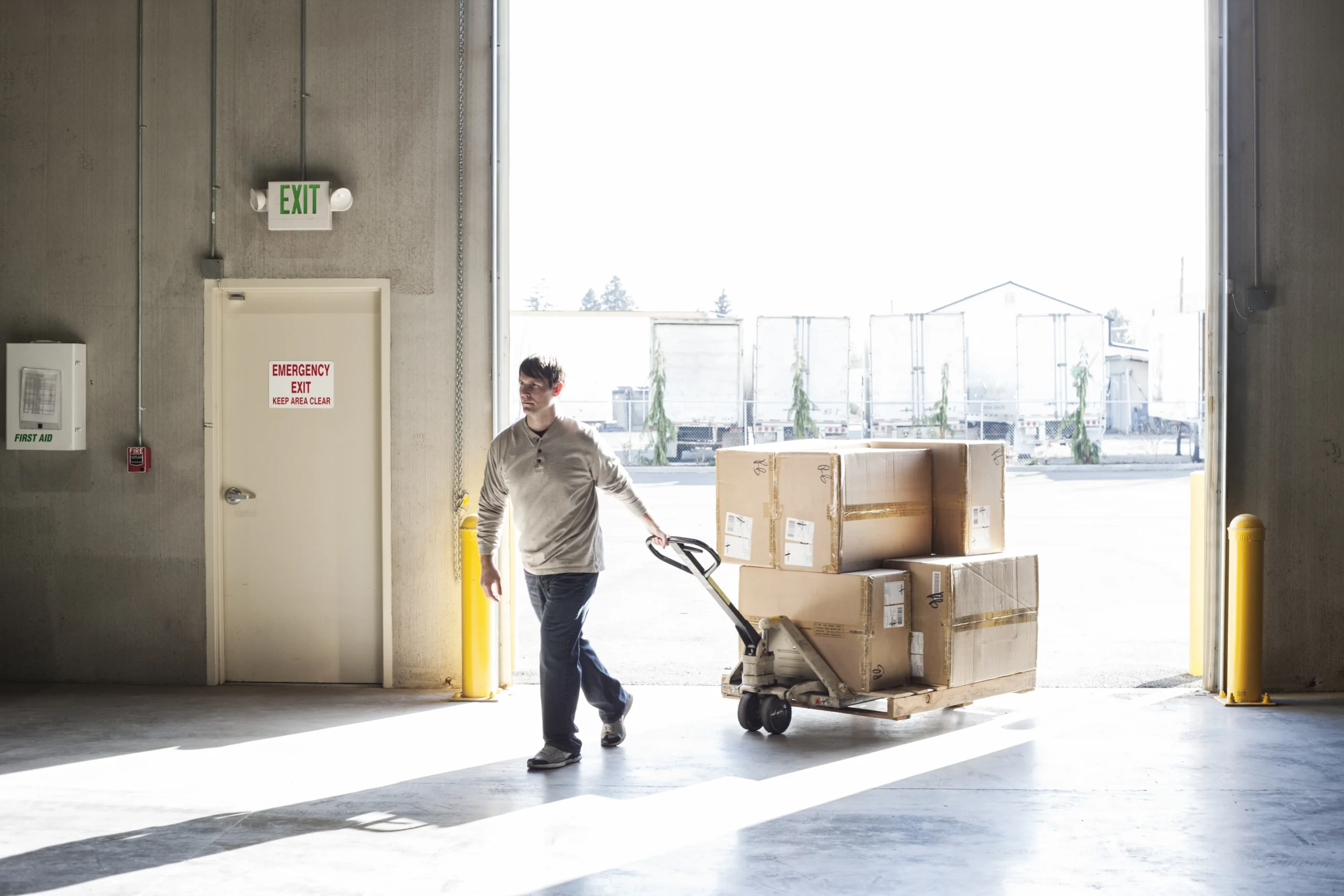 A warehouse worker moving multiple packages using a hand truck, illustrating the high turnover demands of cross-docking operations.