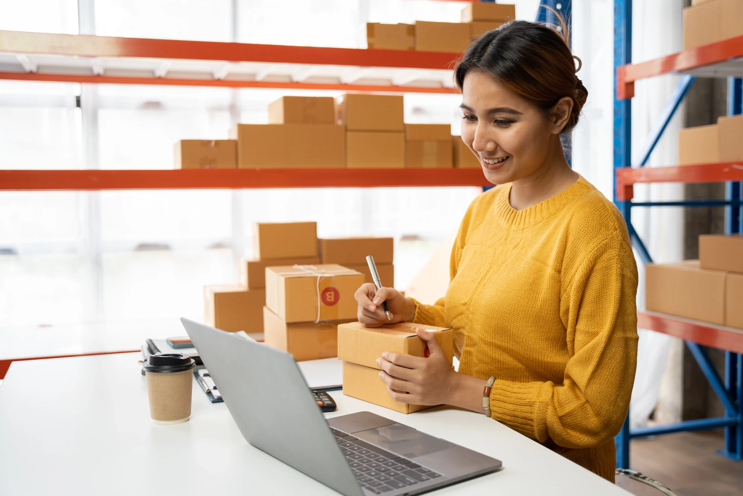 Female entrepreneur preparing e-commerce orders for shipping in a warehouse as part of the order fulfillment process.