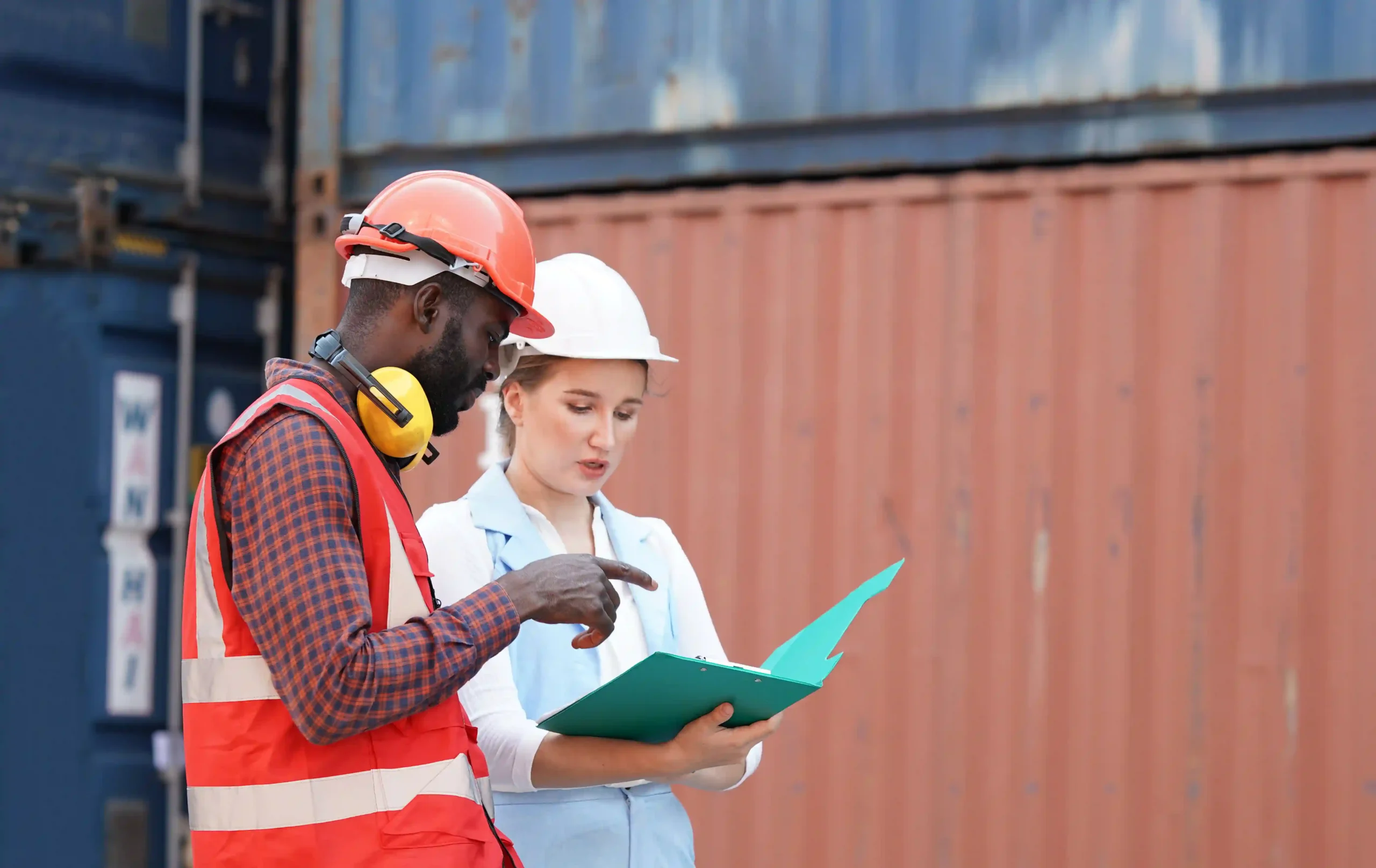 Logistics workers reviewing a customs annual report near cargo containers, ensuring compliance and accurate documentation.