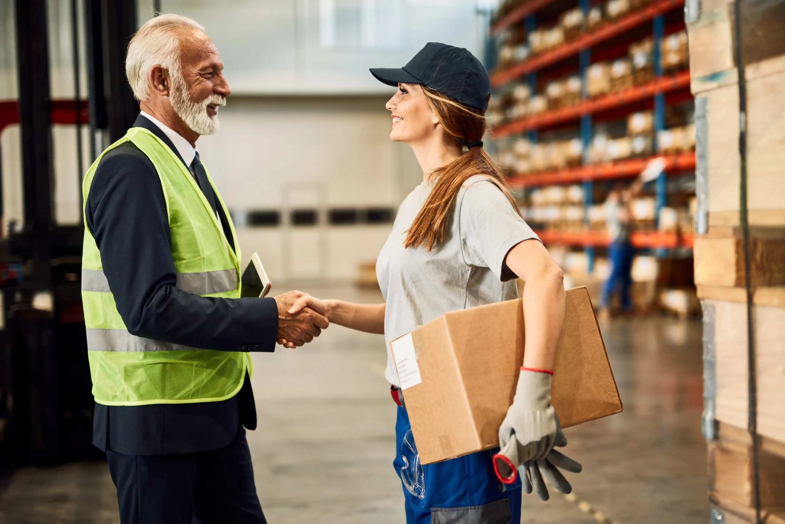 Senior business leader shaking hands with a warehouse worker, symbolizing successful logistics collaboration.