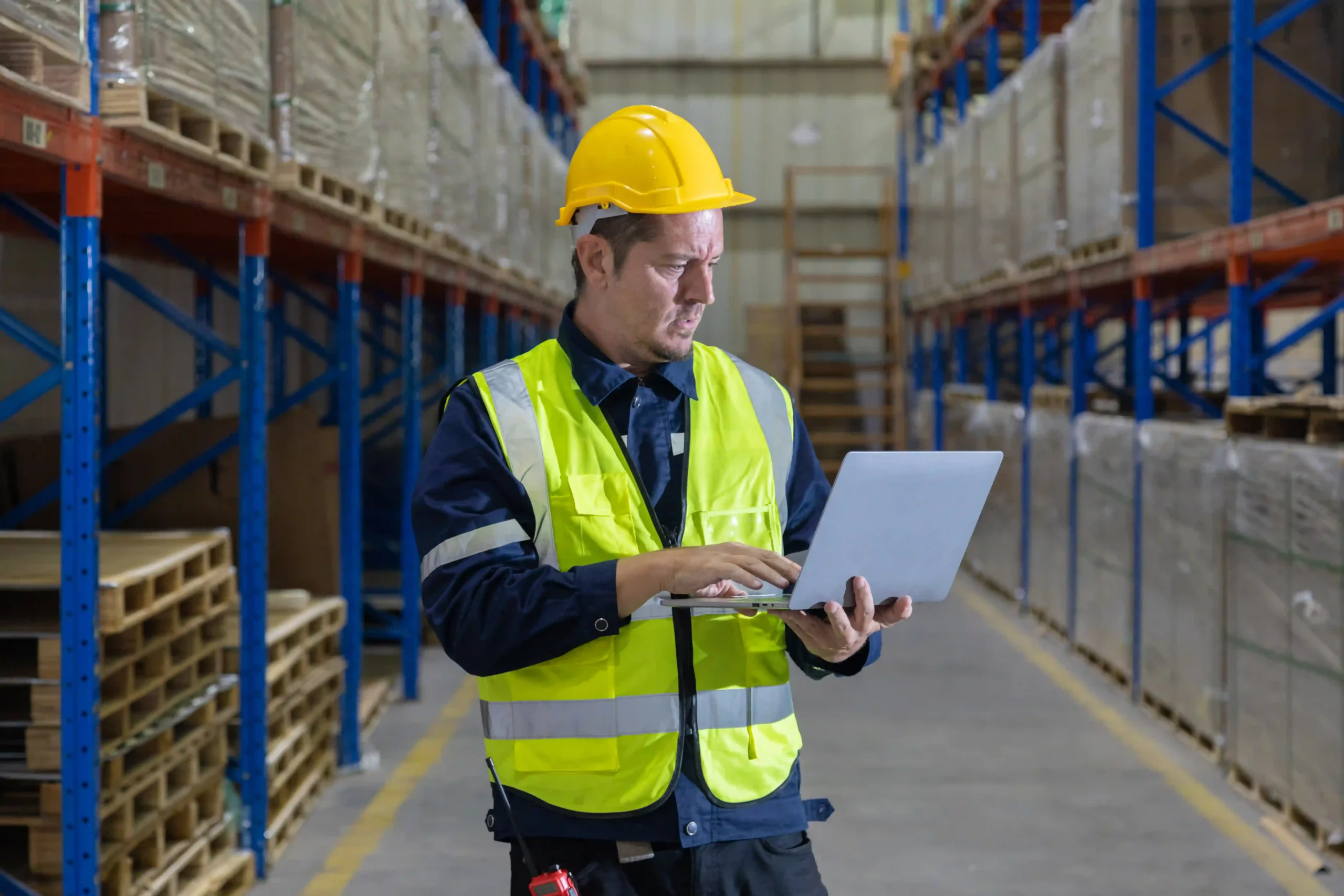 Two warehouse employees reviewing stock inventory with a laptop and clipboard, emphasizing the role of a warehouse management system questionnaire in streamlining warehouse efficiency.