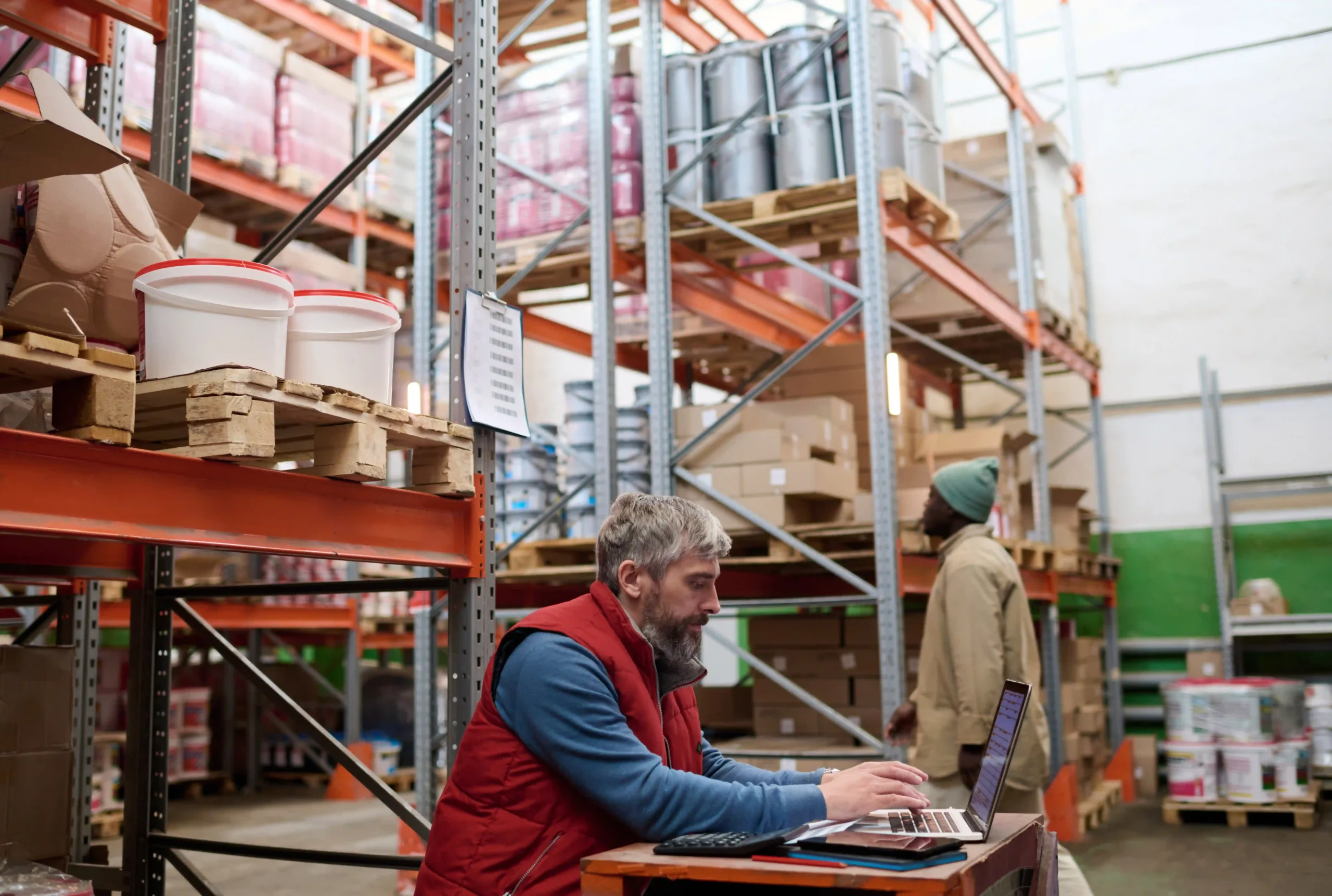 Warehouse supervisor managing stock levels using an inventory management system list on a laptop.