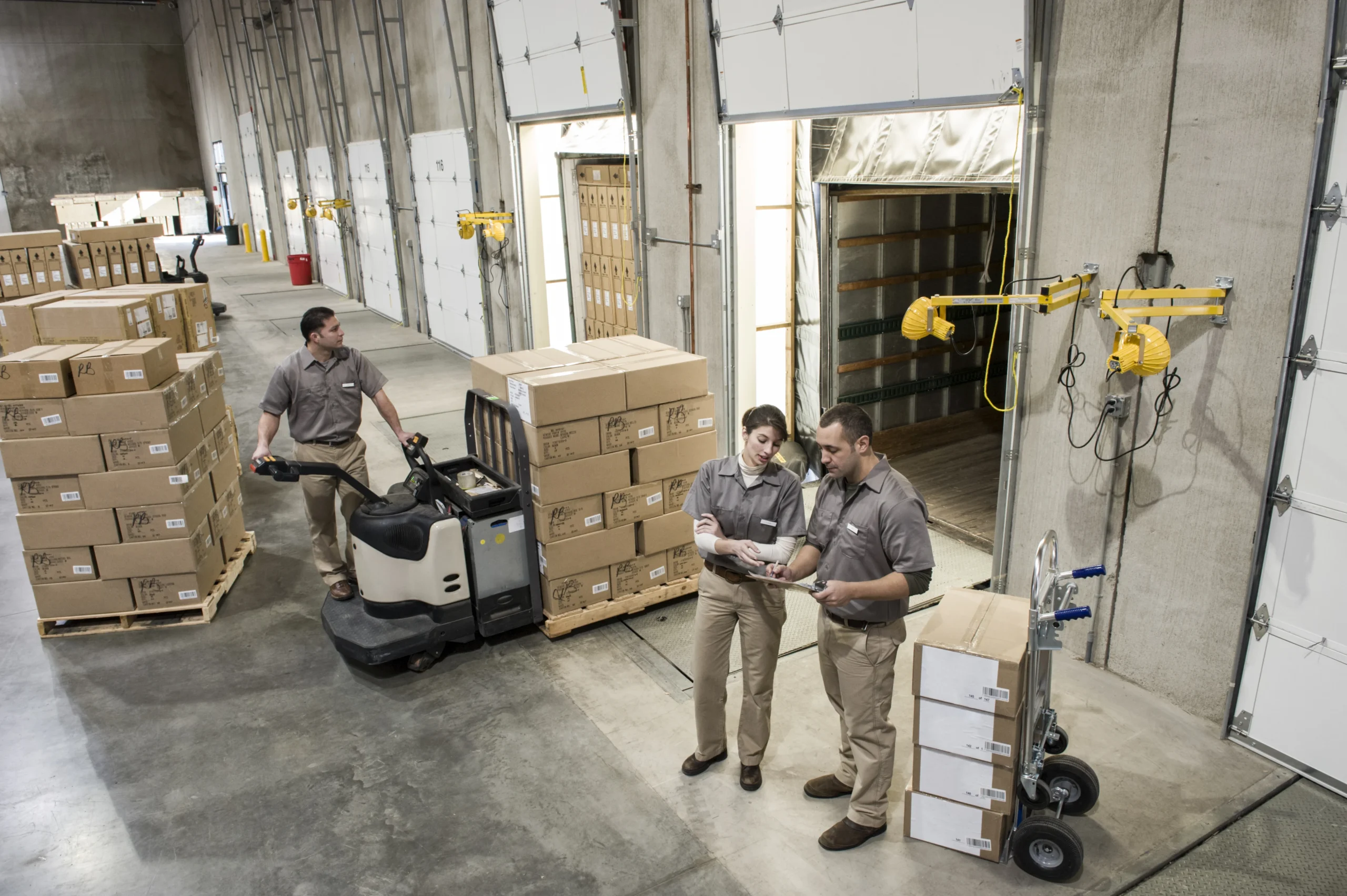 Uniformed warehouse workers preparing boxed products for outbound shipment in a cross-docking facility.
