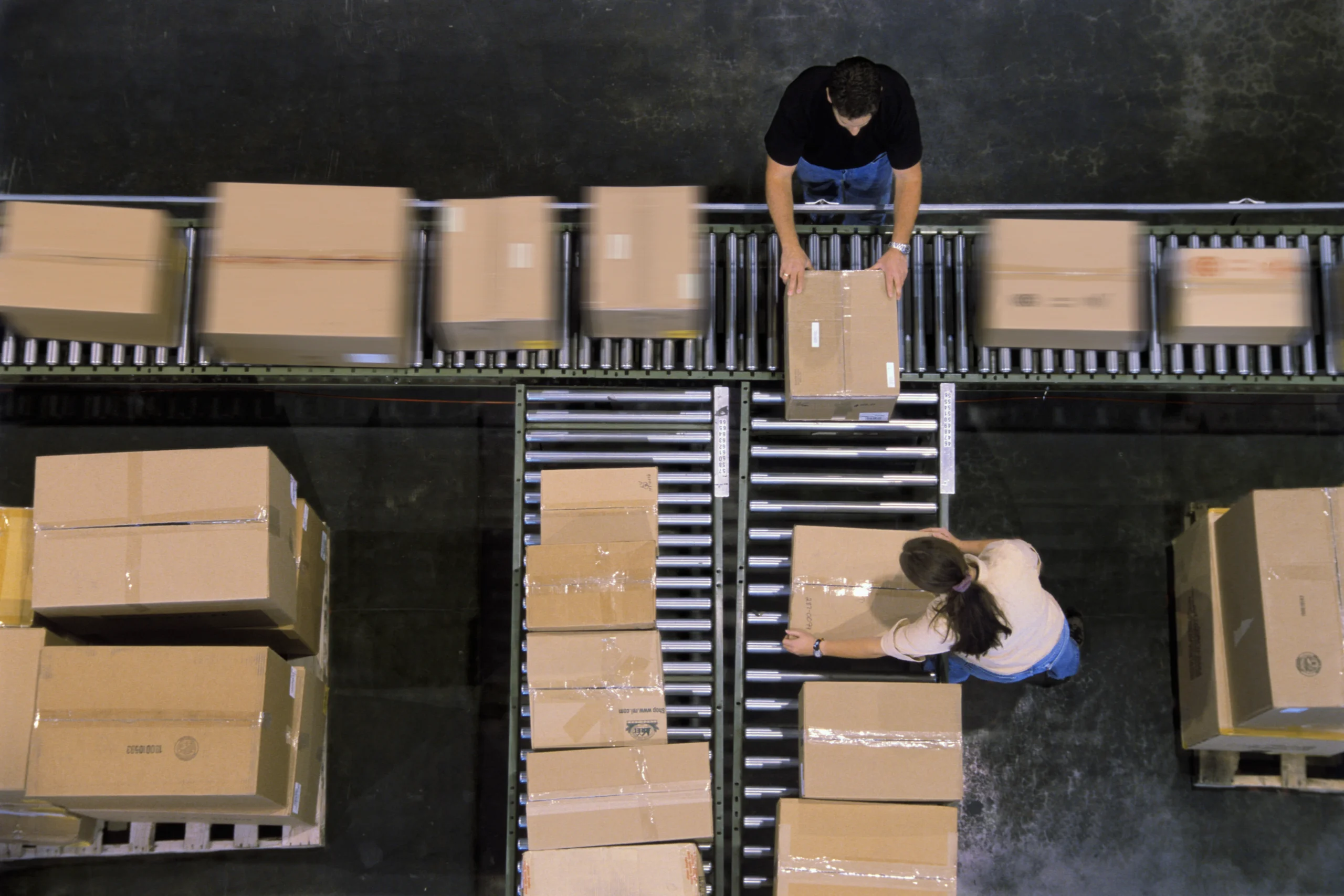 Warehouse employees sorting cardboard boxes on conveyor belts during cross docking operations.