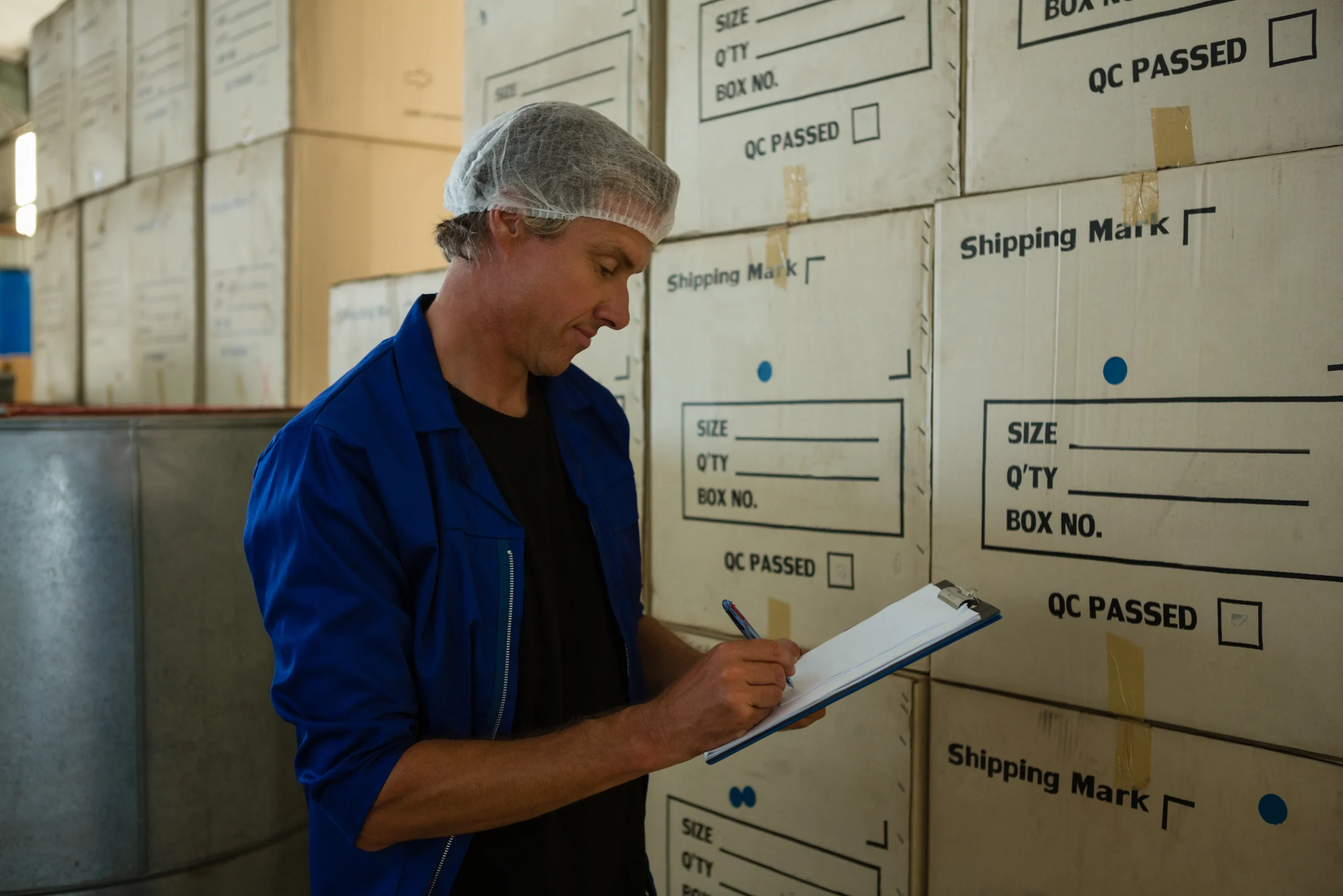 A warehouse worker in a blue uniform using an inventory management system journal to record product details and maintain inventory accuracy.