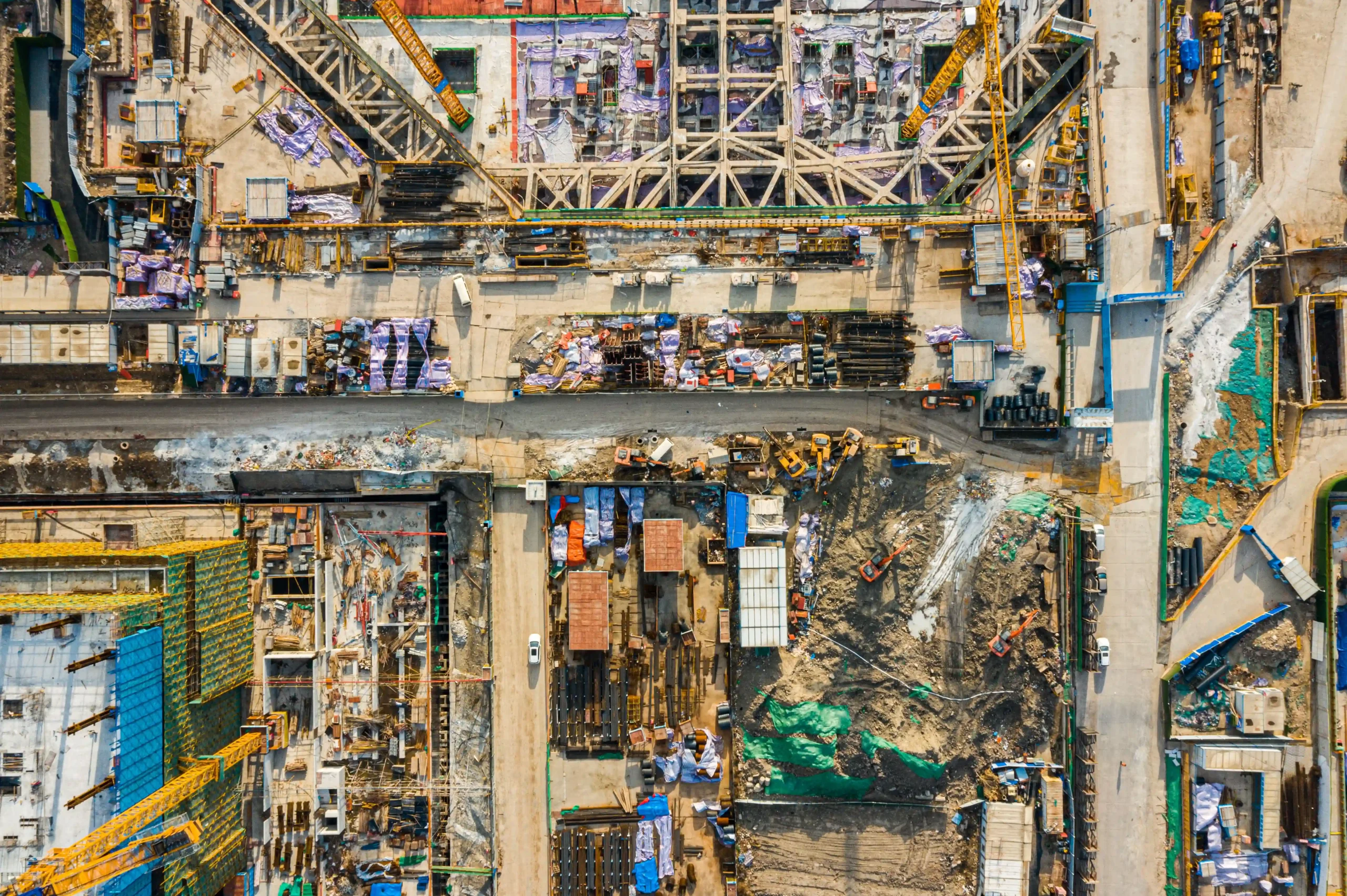 An aerial view of an active construction site representing heavy regulated industries, featuring cranes, equipment, and materials in a highly controlled work environment.