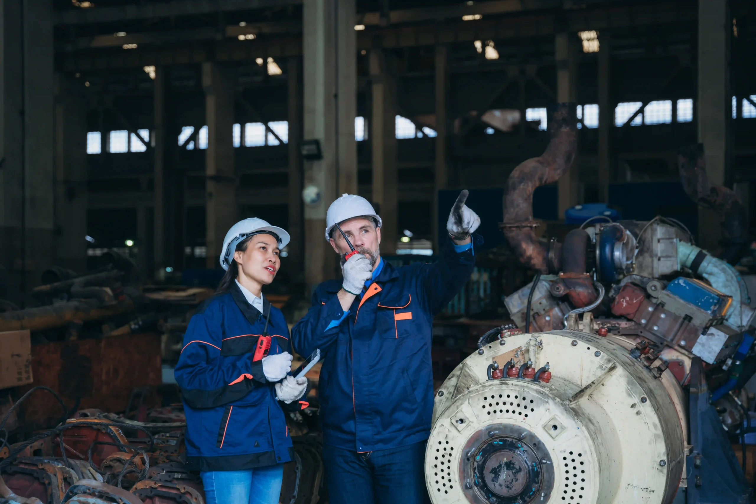 Two engineers in a factory setting discussing equipment and safety procedures, illustrating the challenges and regulations within heavy regulated industries.
