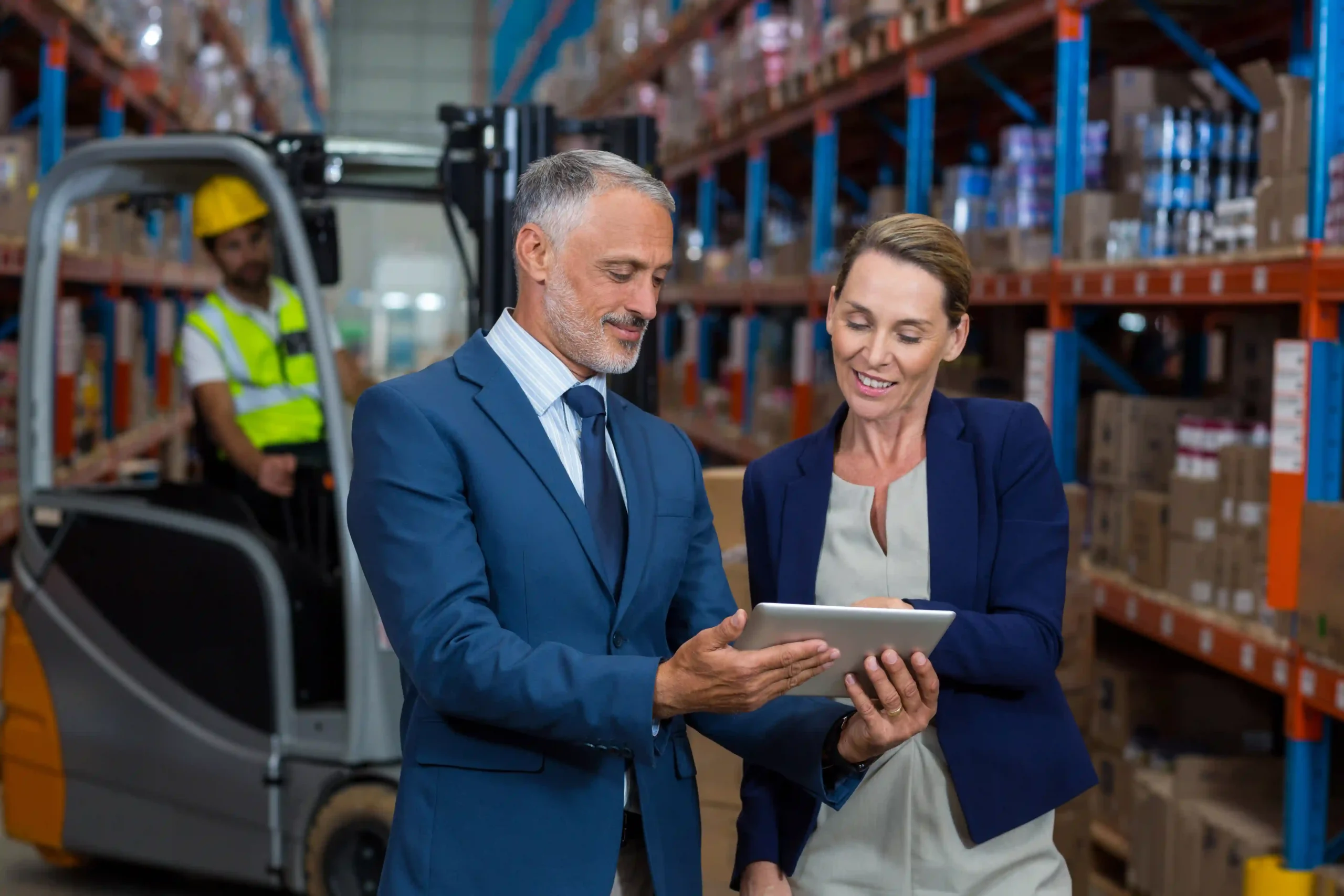 A warehouse manager and a client reviewing logistics on a tablet, showcasing compliance and supply chain management in heavy regulated industries.