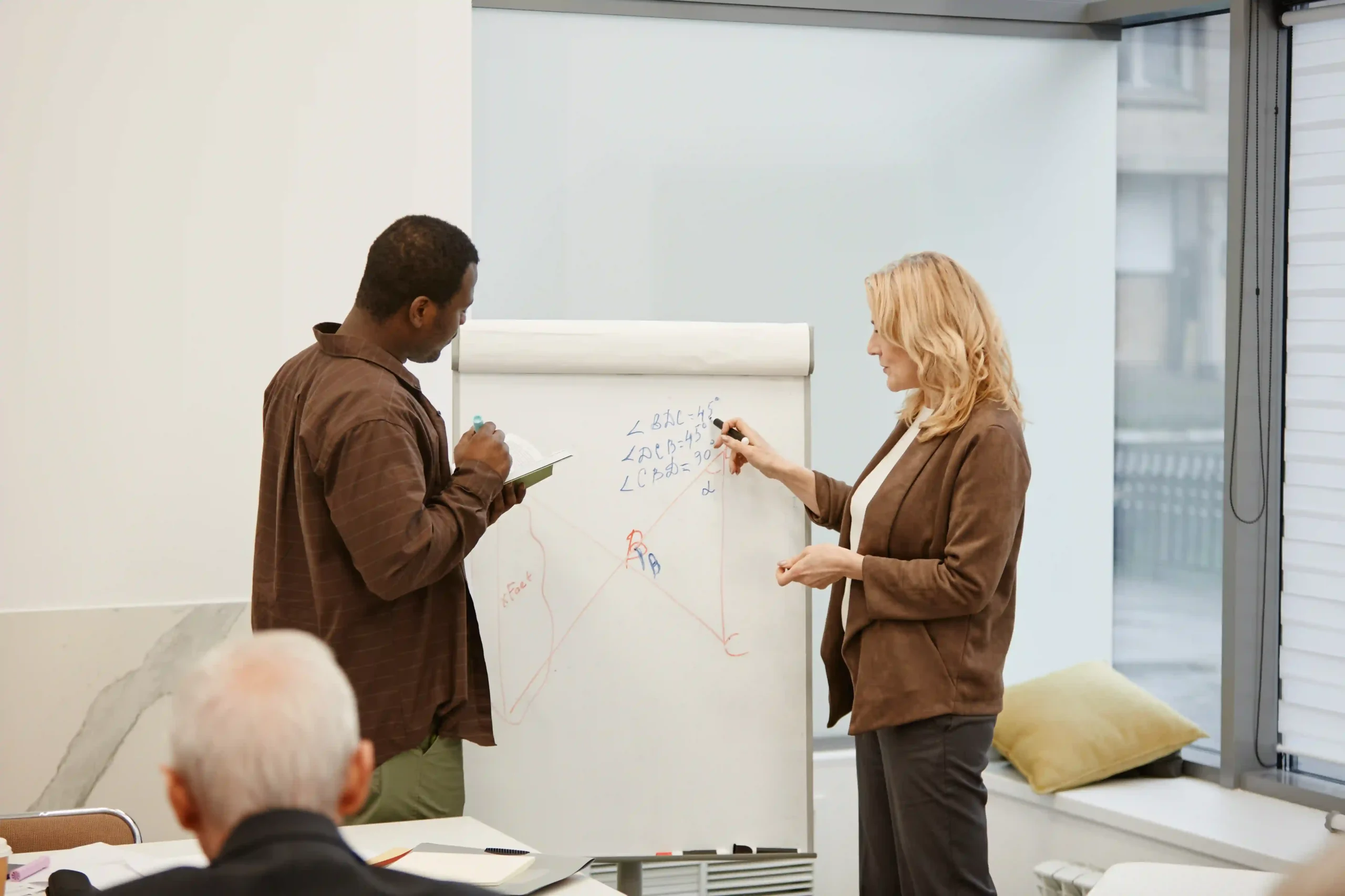 A business professional presenting supply chain optimization training concepts on a flip chart to a group of logistics professionals.