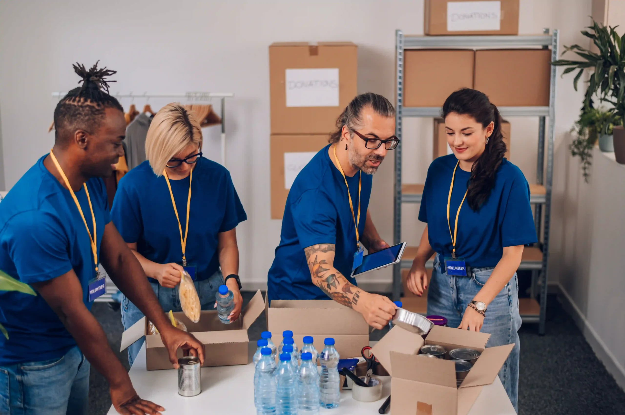 A diverse team of volunteers wearing blue shirts packing food and water into boxes, representing the pick pack meaning in a simplified community setting.