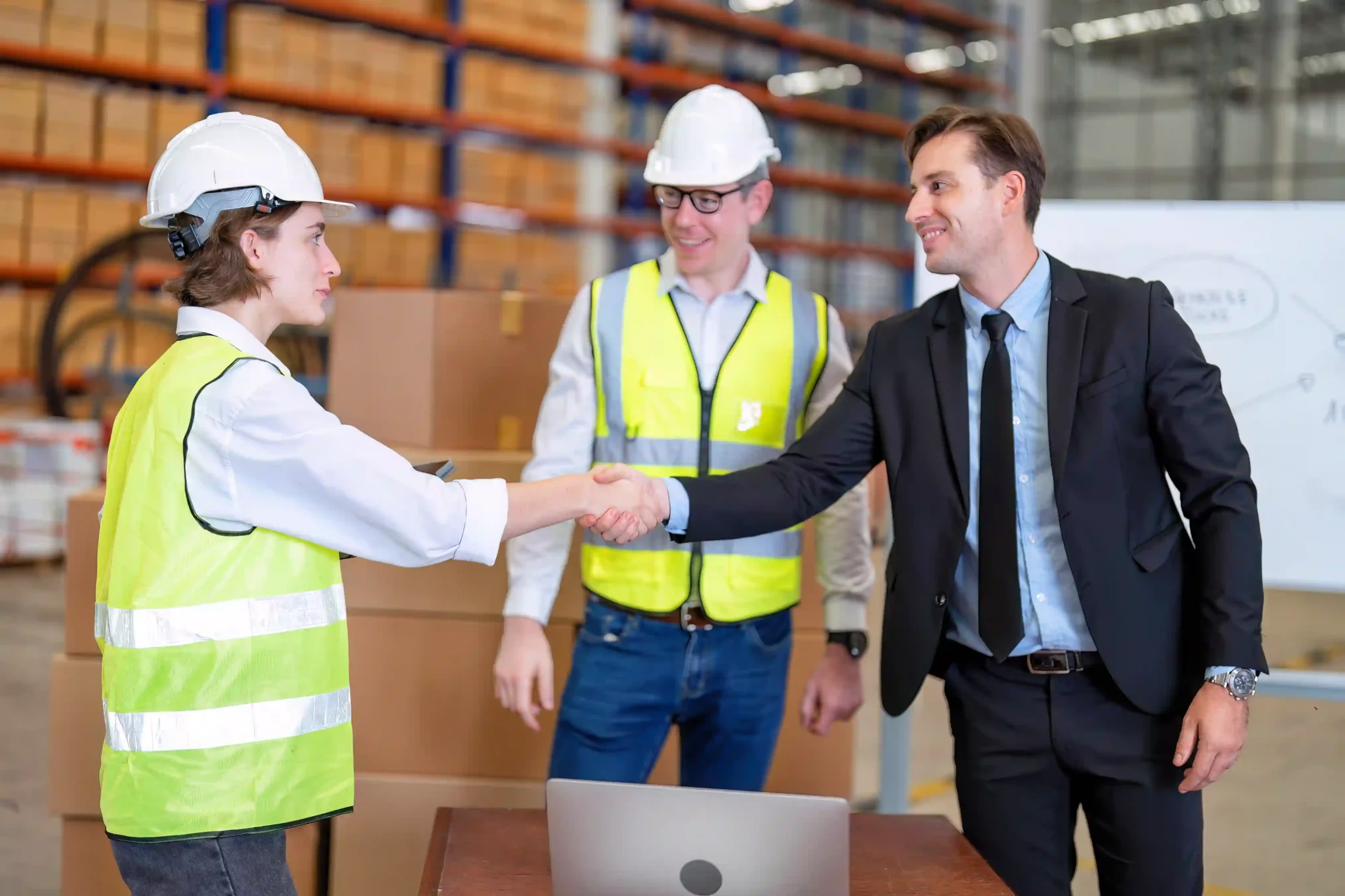 A 3pl logistics manager shakes hands with a warehouse supervisor during a logistics meeting inside a distribution center.