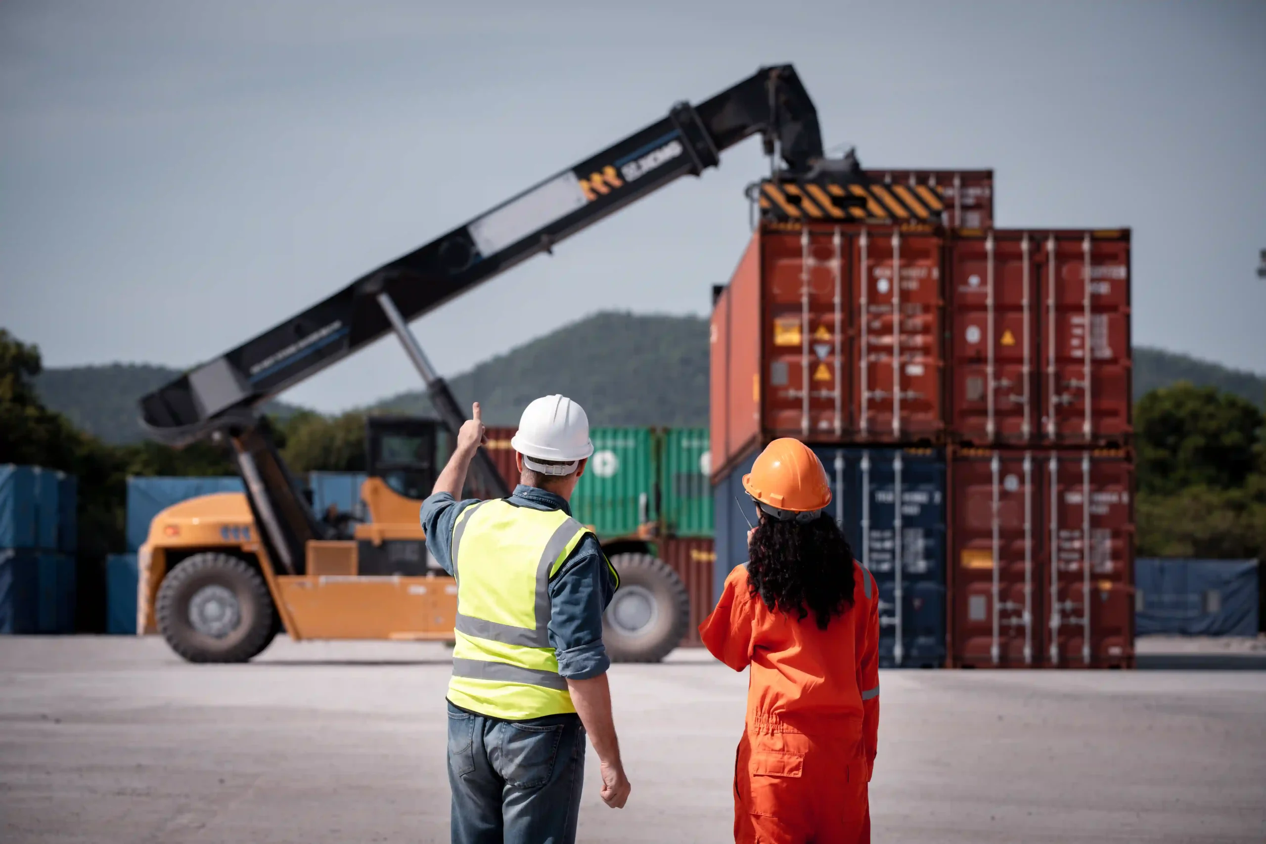 Logistics engineers supervising container stacking with a forklift, showcasing freight logistics and its role in modern logistics management types.