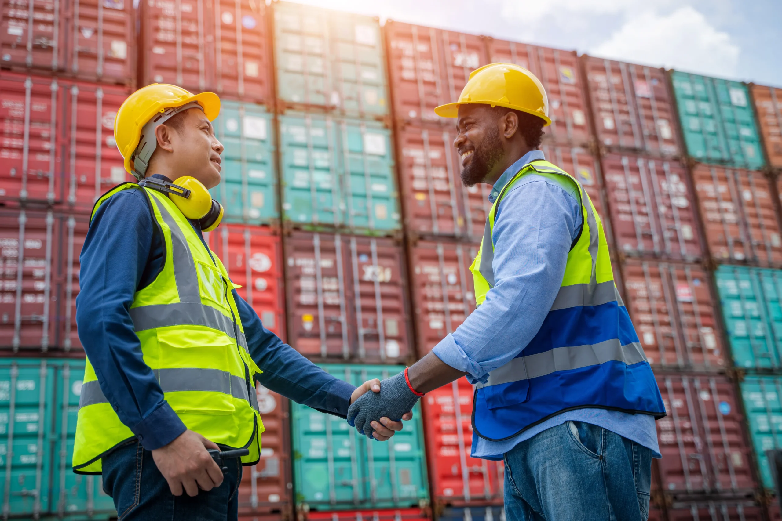 Two export professionals shaking hands in front of stacked shipping containers, symbolizing trade compliance management collaboration
