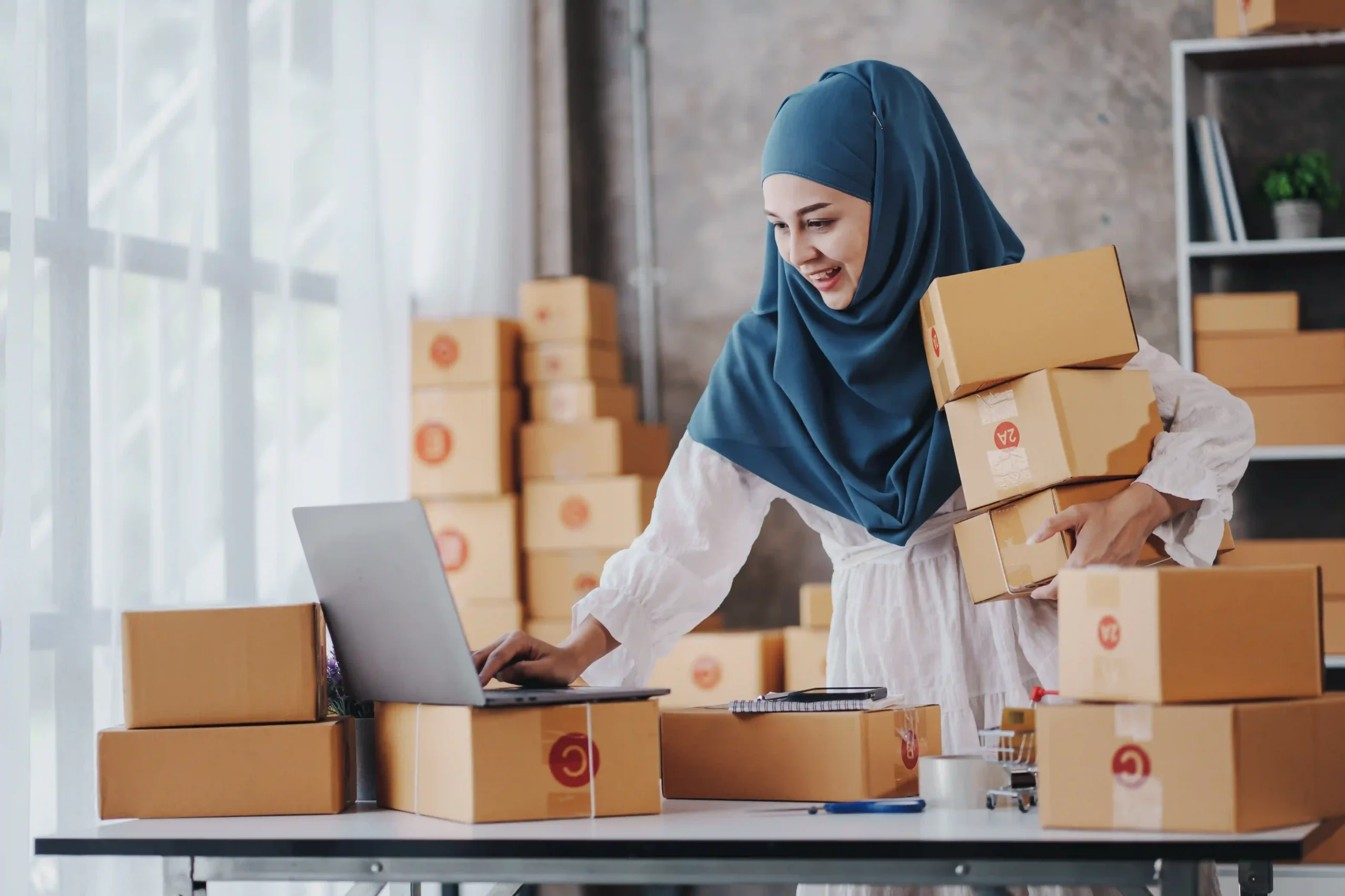 Muslim woman managing ecommerce fulfillment by checking online orders and packing parcels.