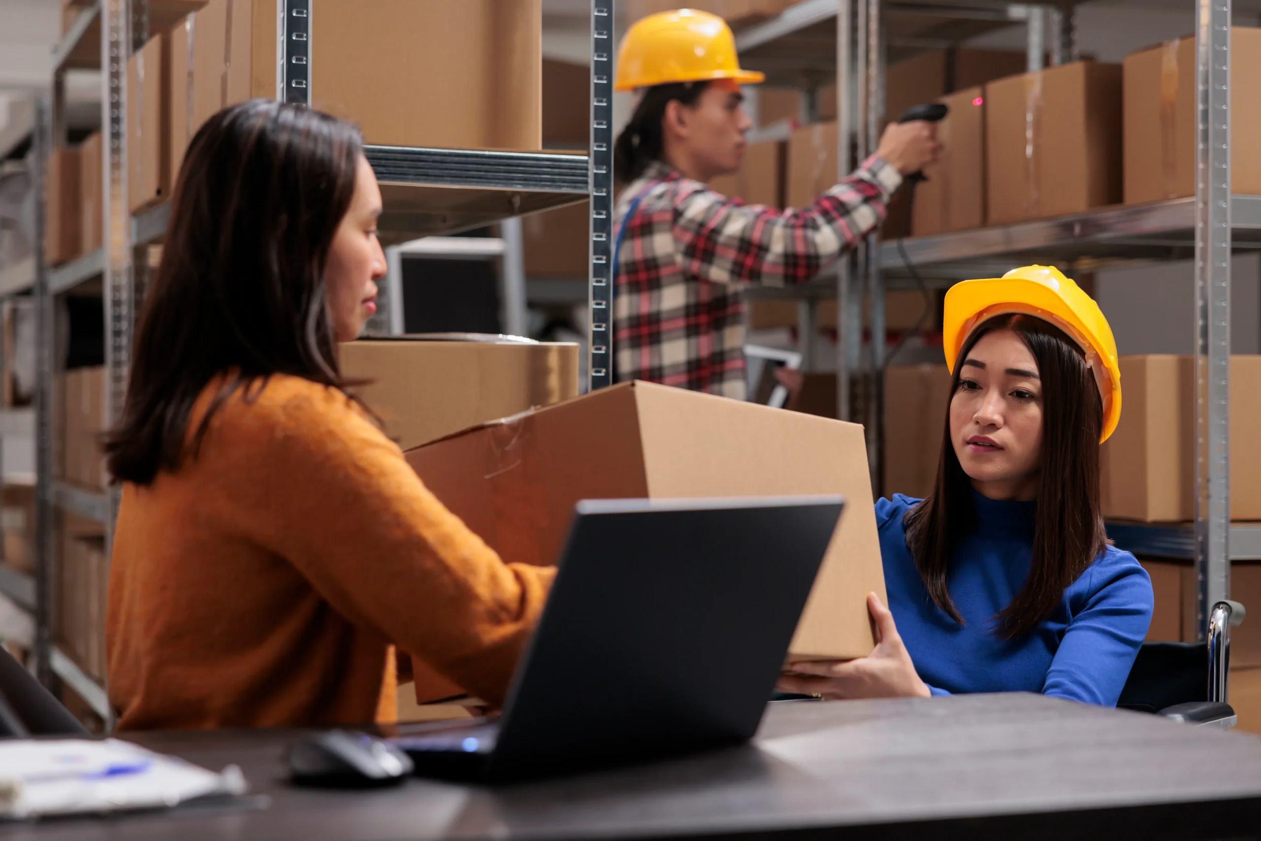 Two women collaborating on supply chain management work while handling packages in a warehouse environment.