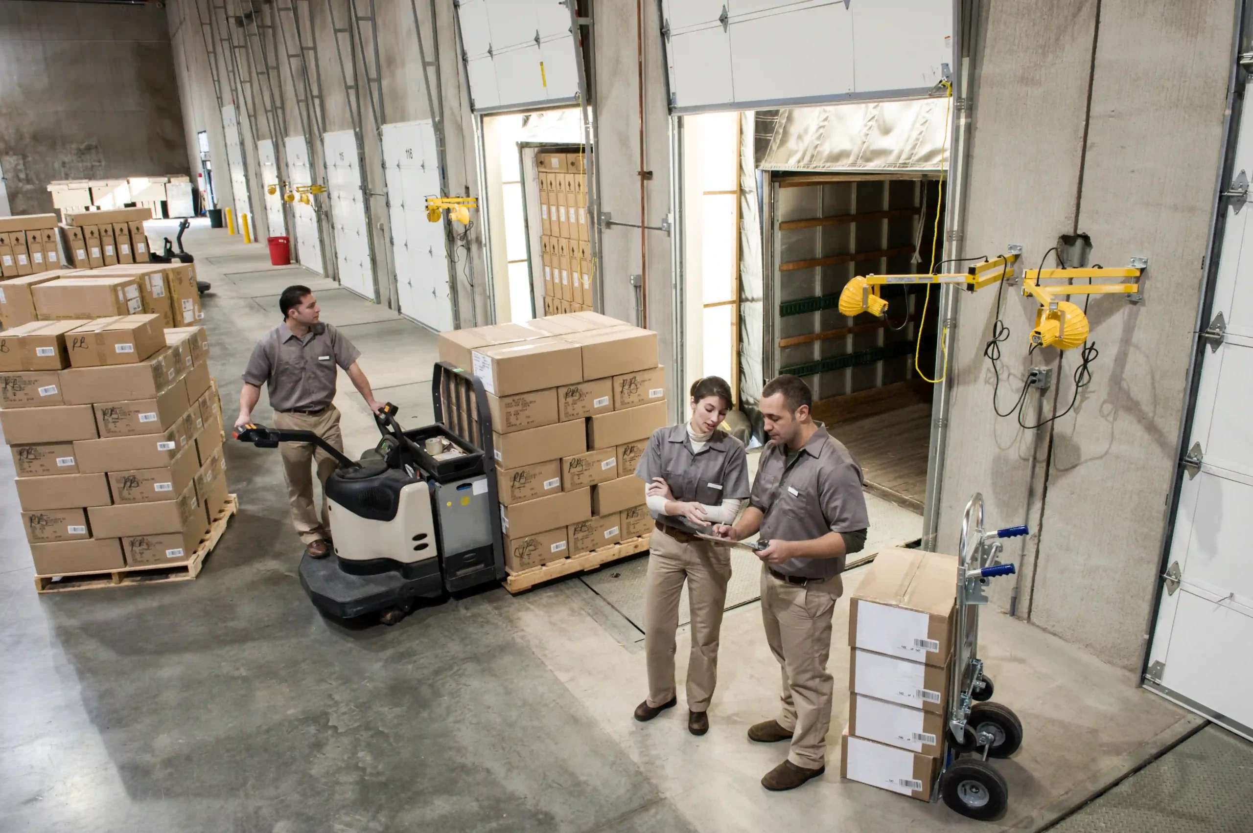 Warehouse workers using pallet jack and digital tools to manage shipments, supported by logistics tracking services.