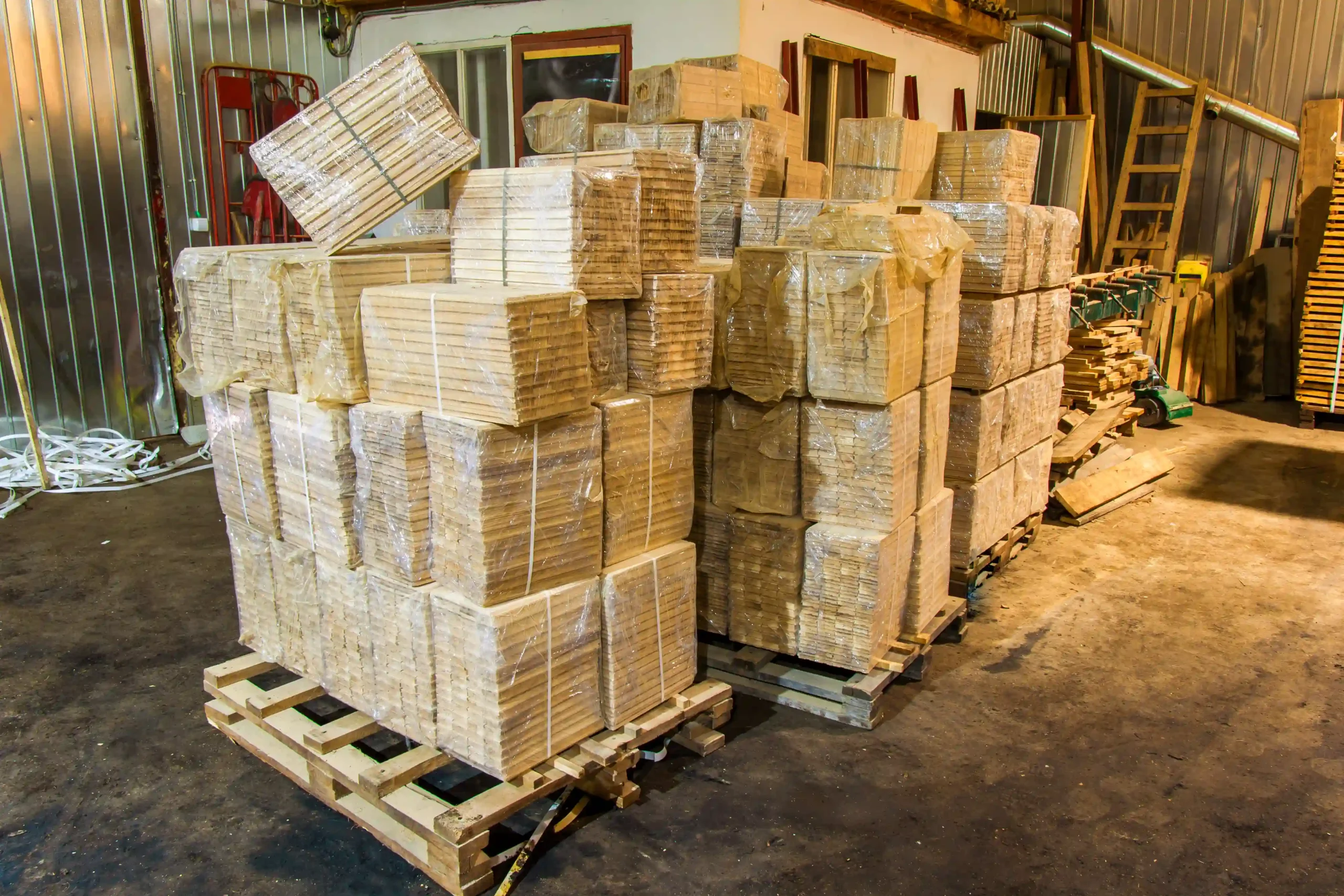 Stacks of shrink-wrapped wood panels on pallets inside a pallet rack warehouse and supply facility.