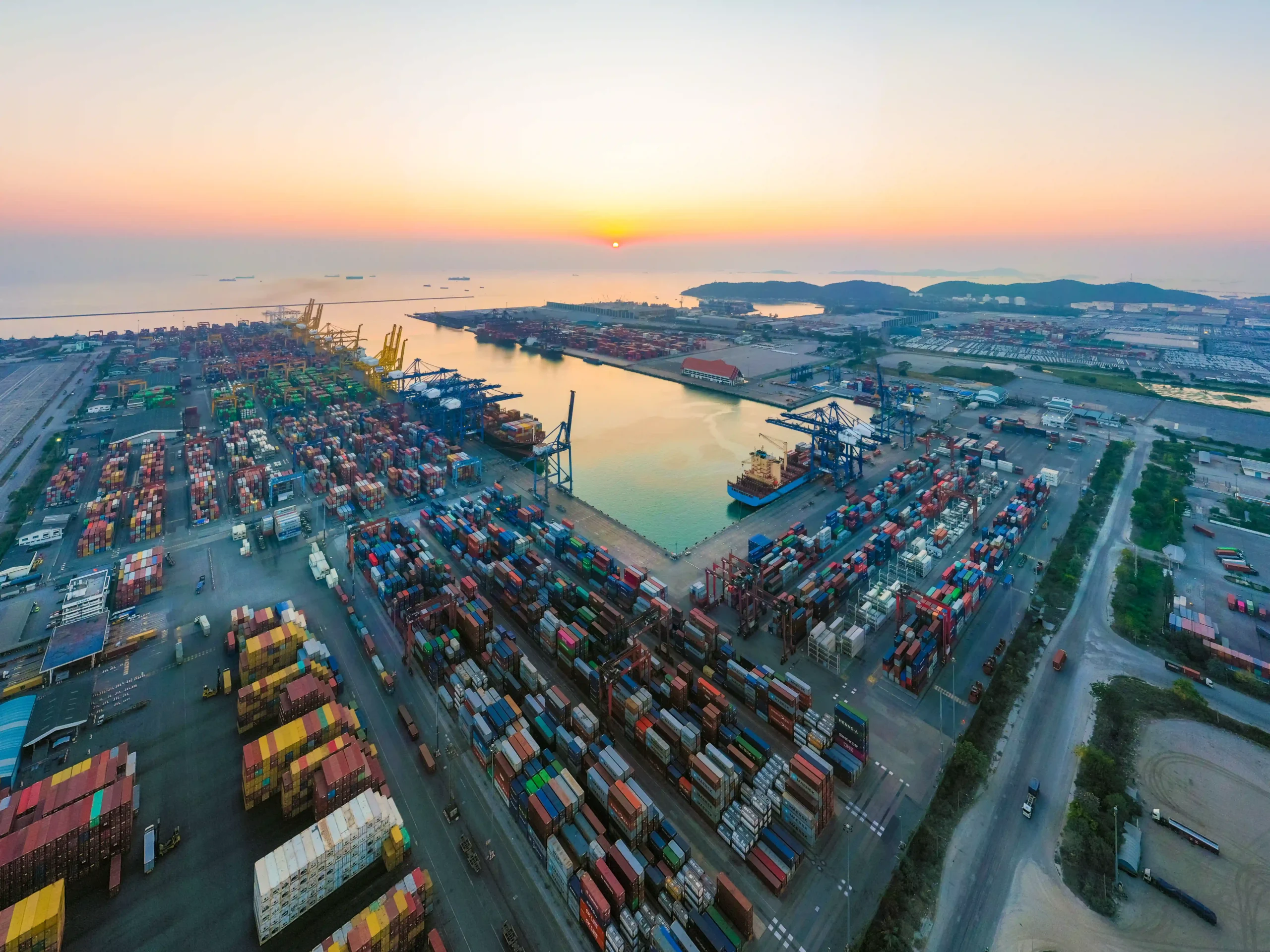 Aerial view of a busy FTZ logistics port at sunset, showcasing containers and cargo ship terminals