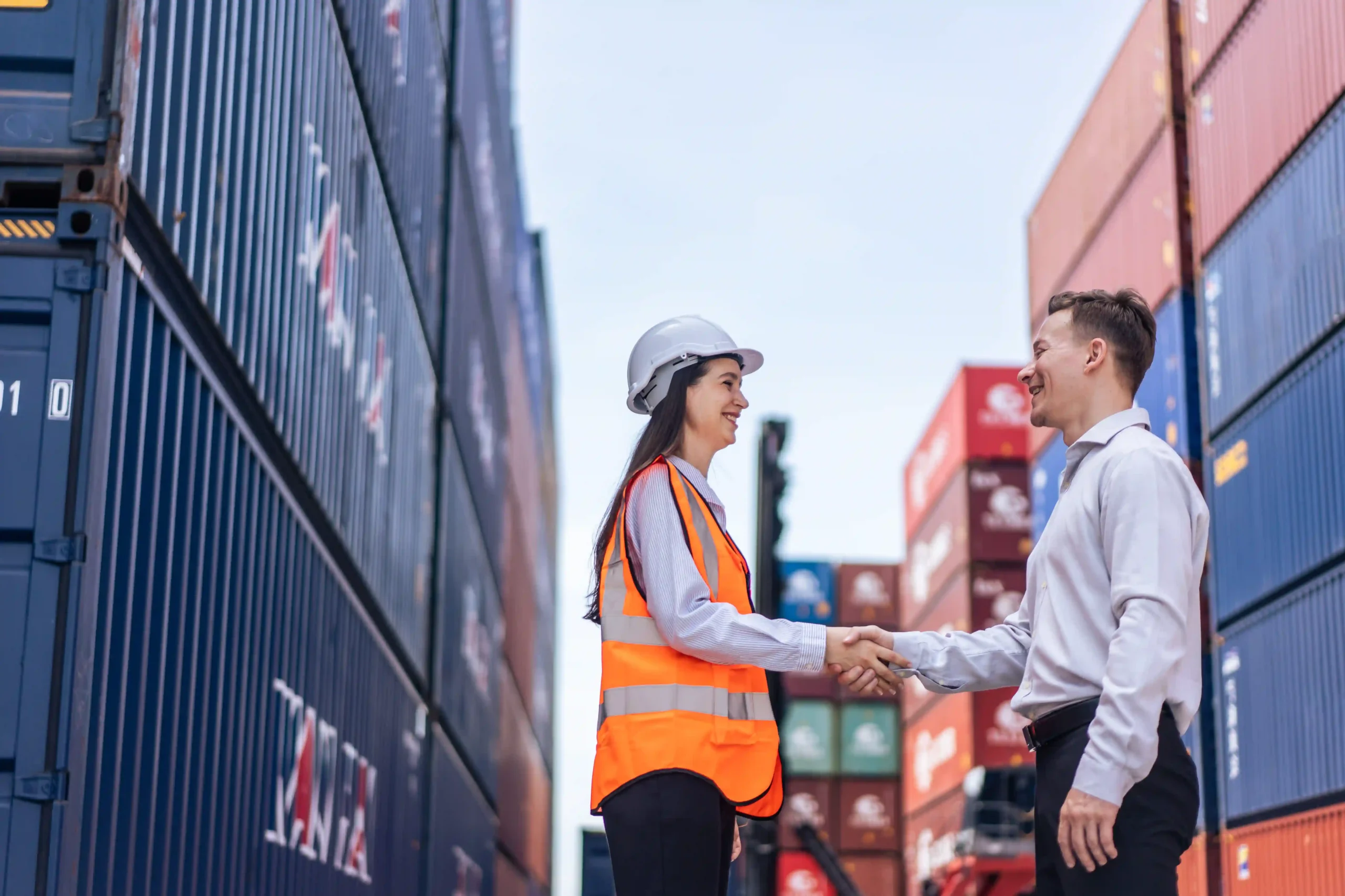 Businesswoman and logistics manager shaking hands near shipping containers at a forwarding company location