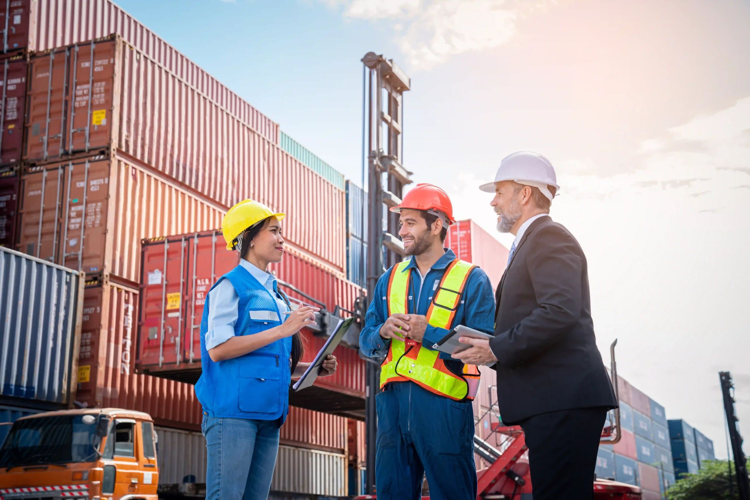 Three logistics professionals collaborating in a container yard, representing value added jobs in the supply chain.