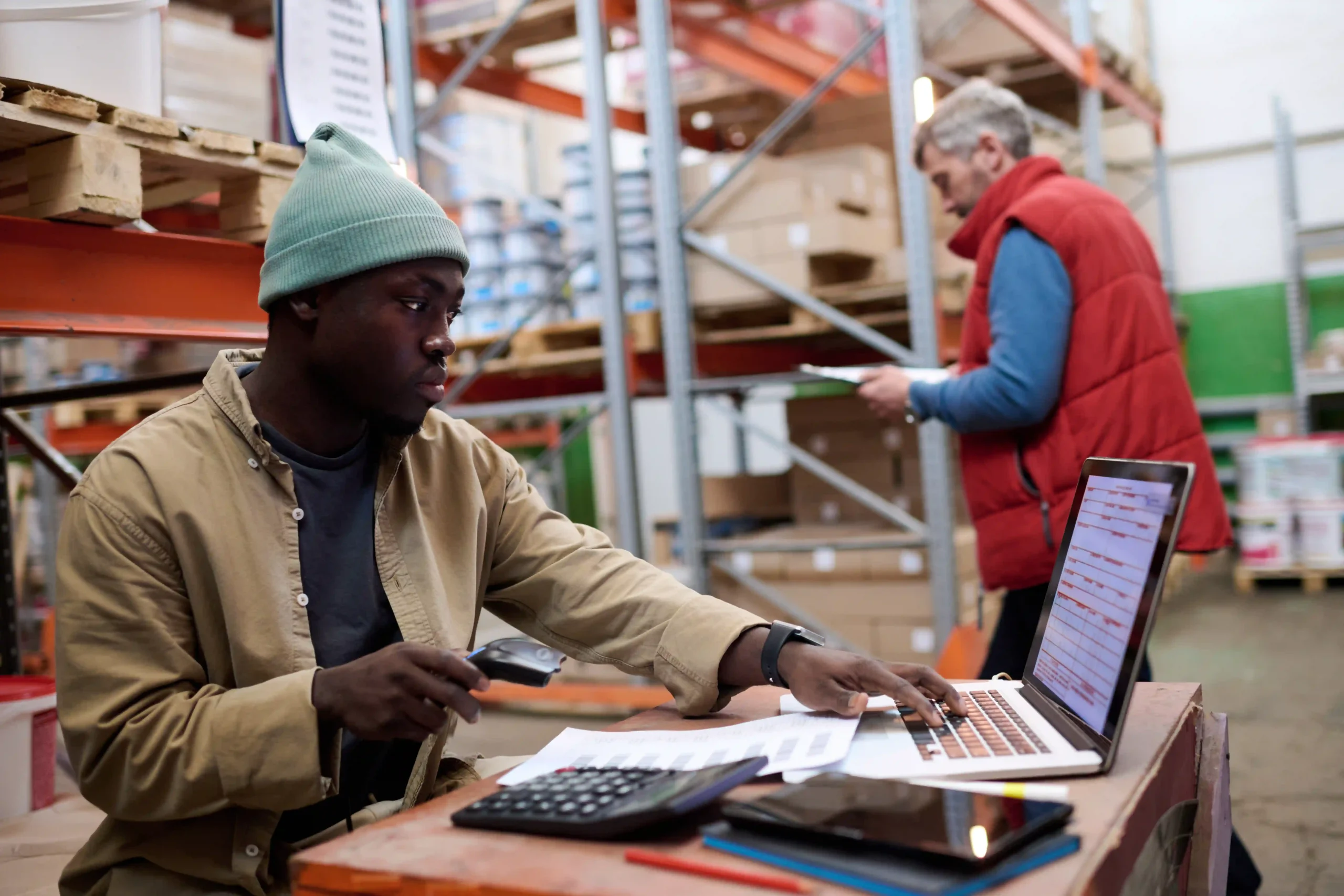 Warehouse worker using laptop and scanner to manage product data during inventory management 101 tasks
