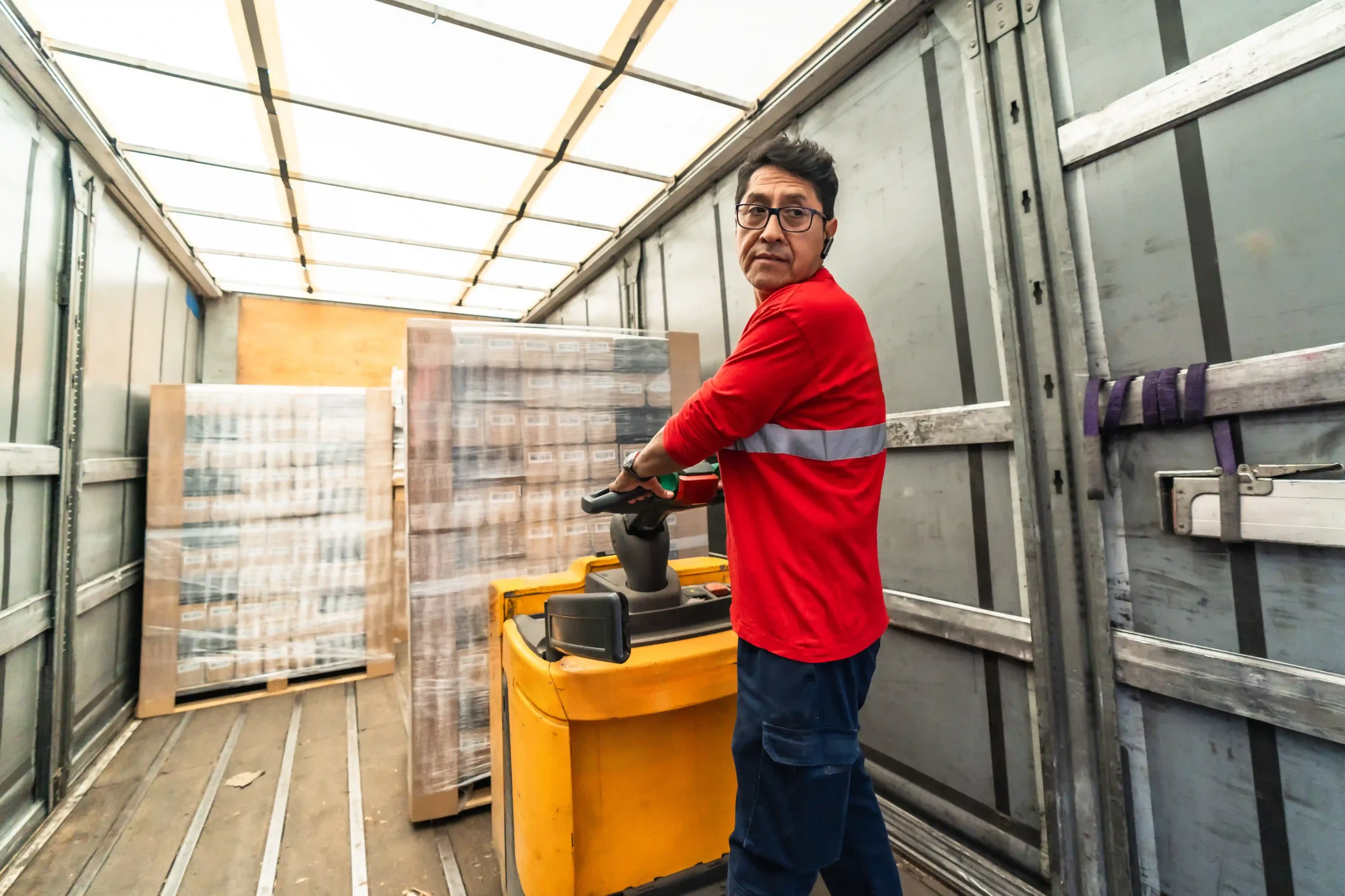 Logistics worker loading freight with a pallet jack using a pallet delivery app system