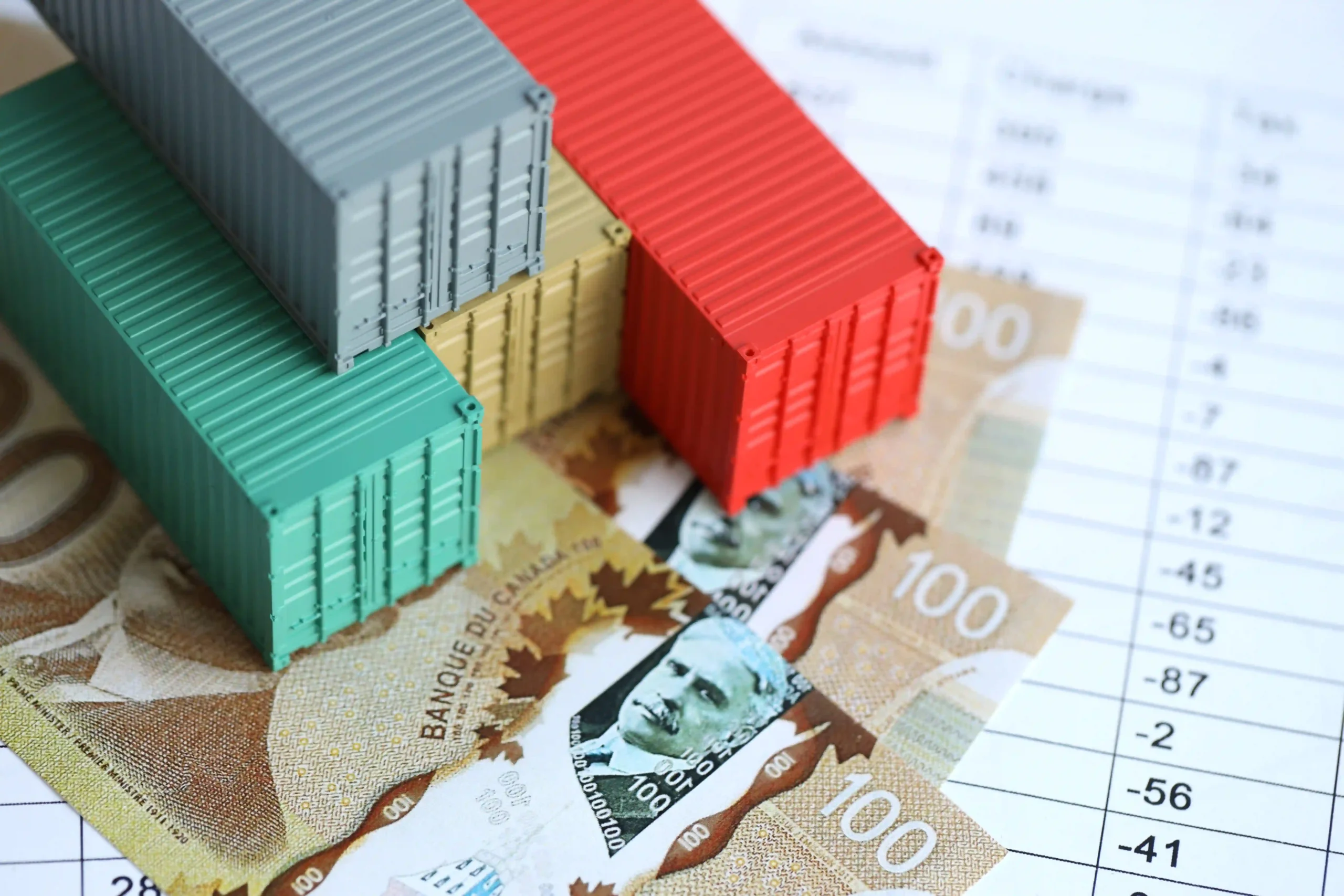 Cargo containers stacked on Canadian banknotes representing cost impacts of de minimis Canada to US suspension.