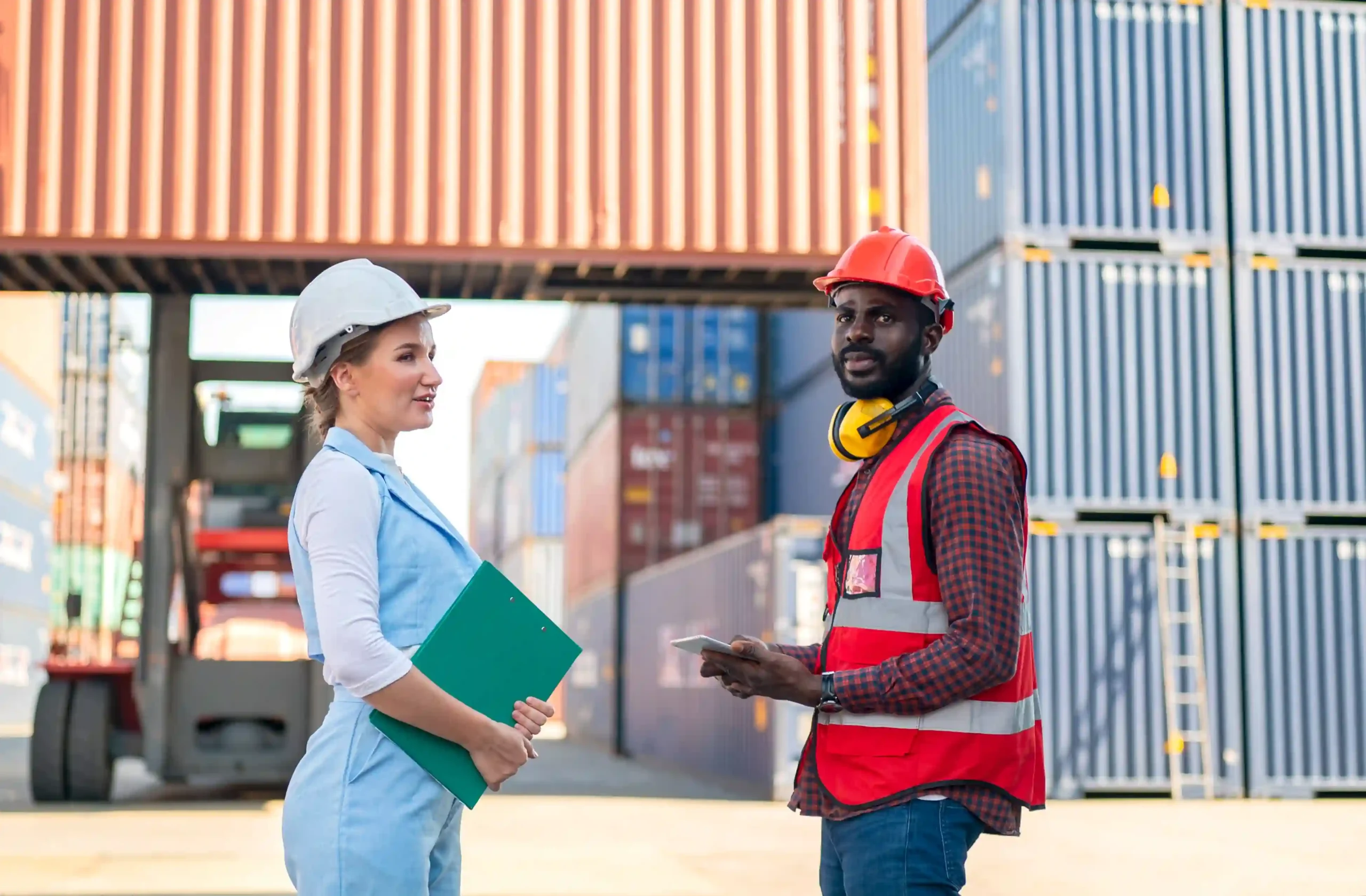 Logistics foreman and worker discuss shipments impacted by the de minimis trade loophole near stacked containers.