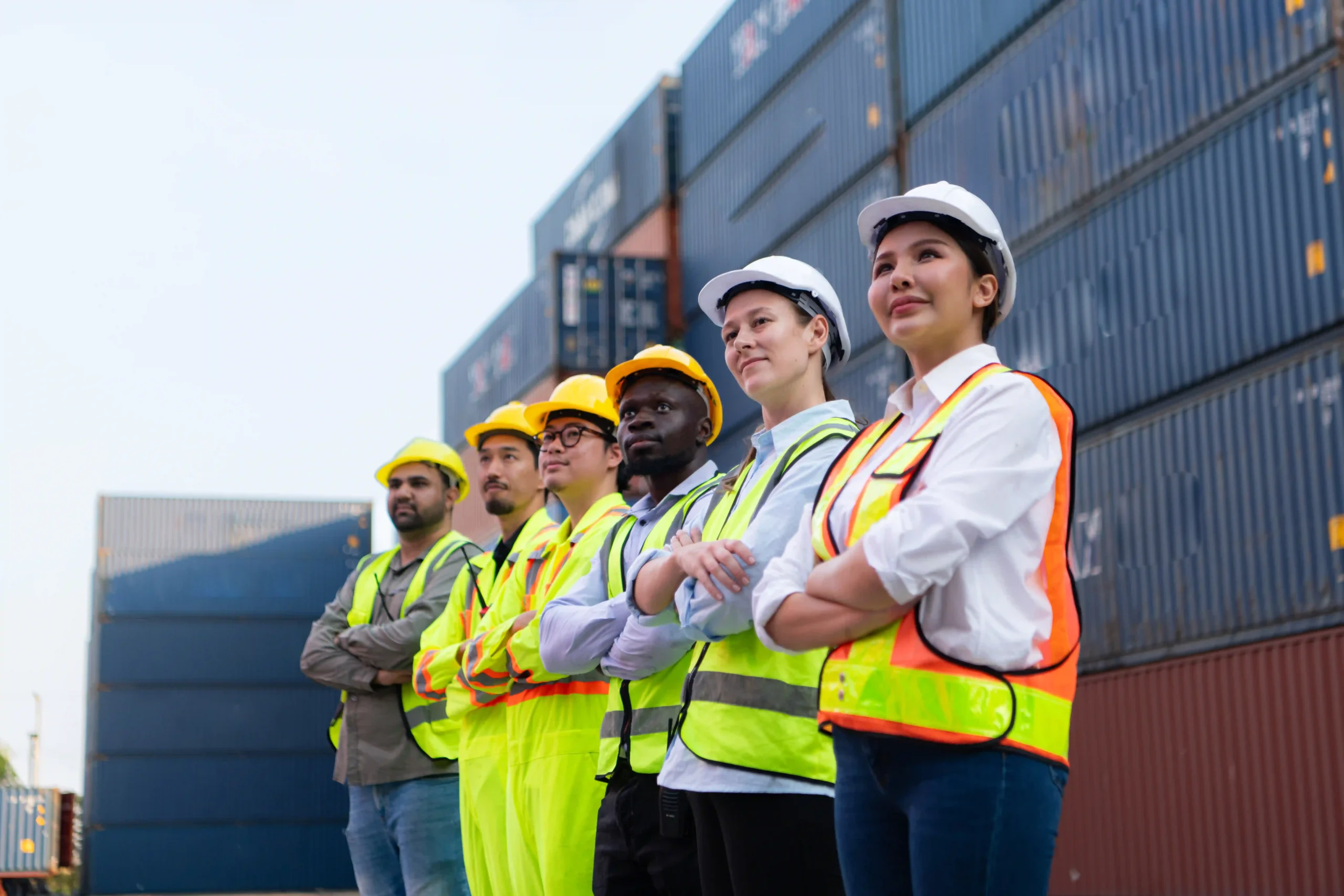 Diverse logistics team wearing safety vests and helmets at a shipping port, showing unity in adapting to de minimis tariffs.