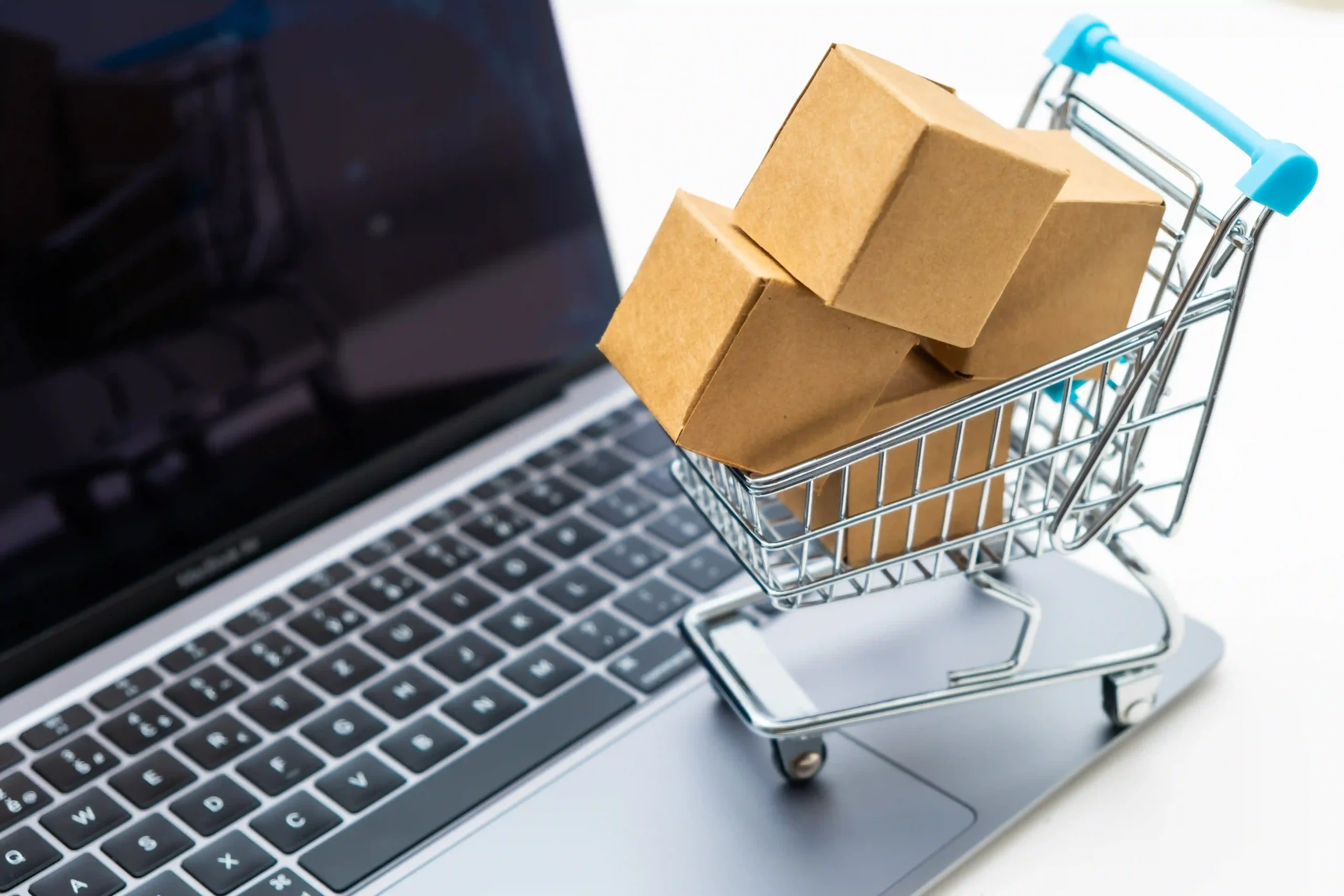 Small cardboard boxes in shopping cart on laptop illustrate online shipping and the de minimis standard in trade.