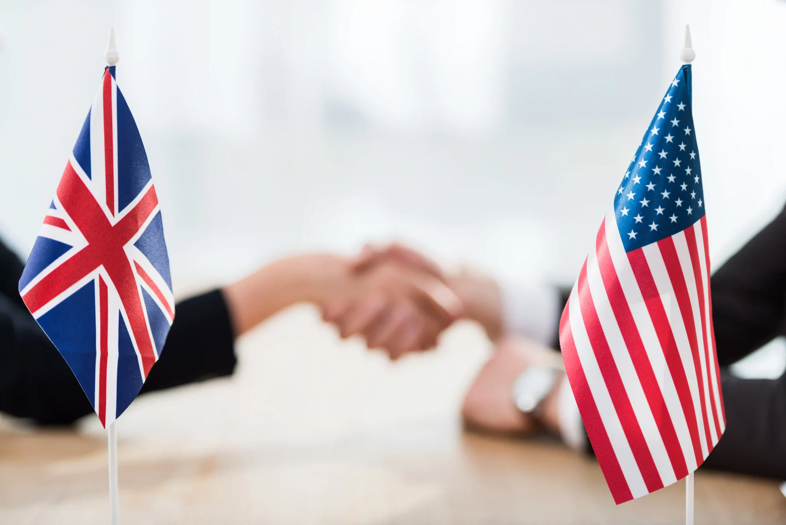 Business handshake with UK and U.S. flags reflecting partnerships and logistics after de minimis UK to USA changes.