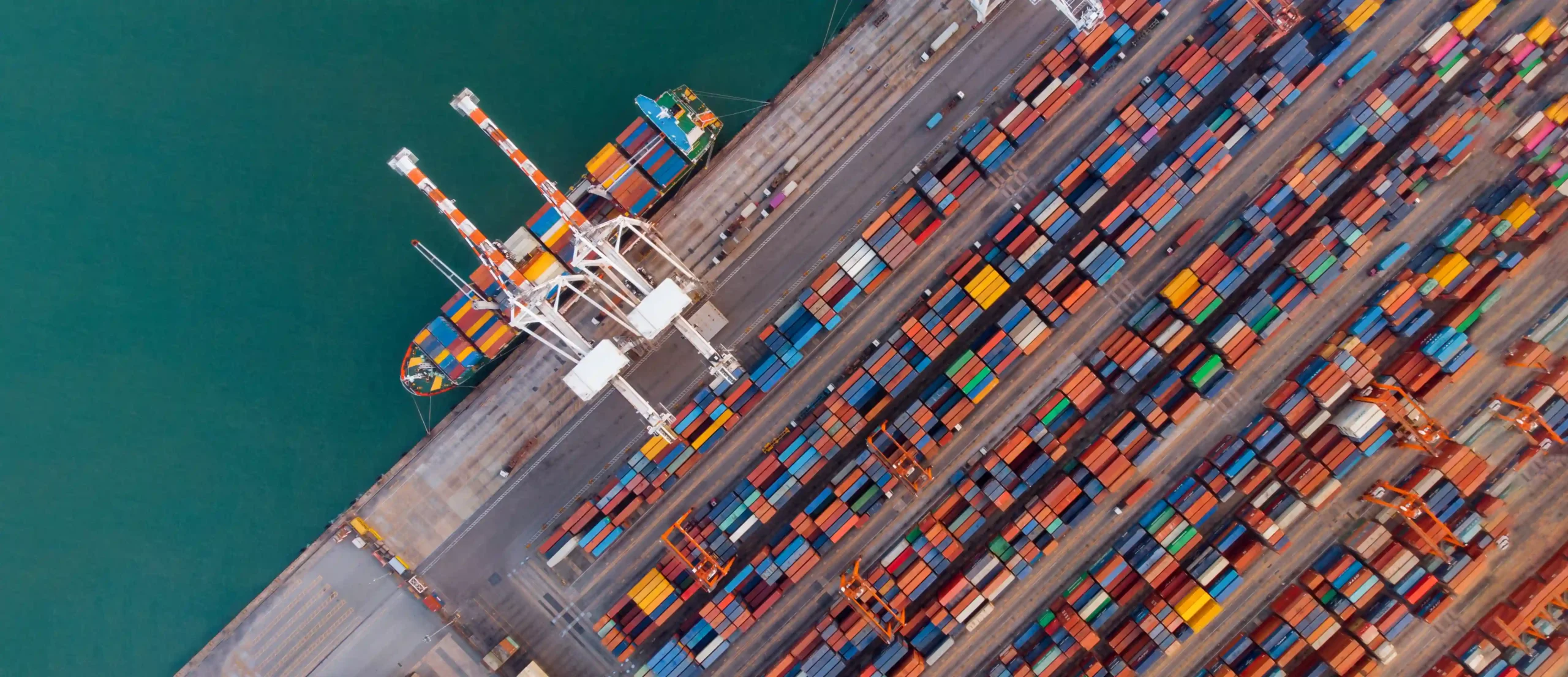 Aerial view of cargo containers and cranes at a busy shipping port representing global trade shifts during the de minimis transition.