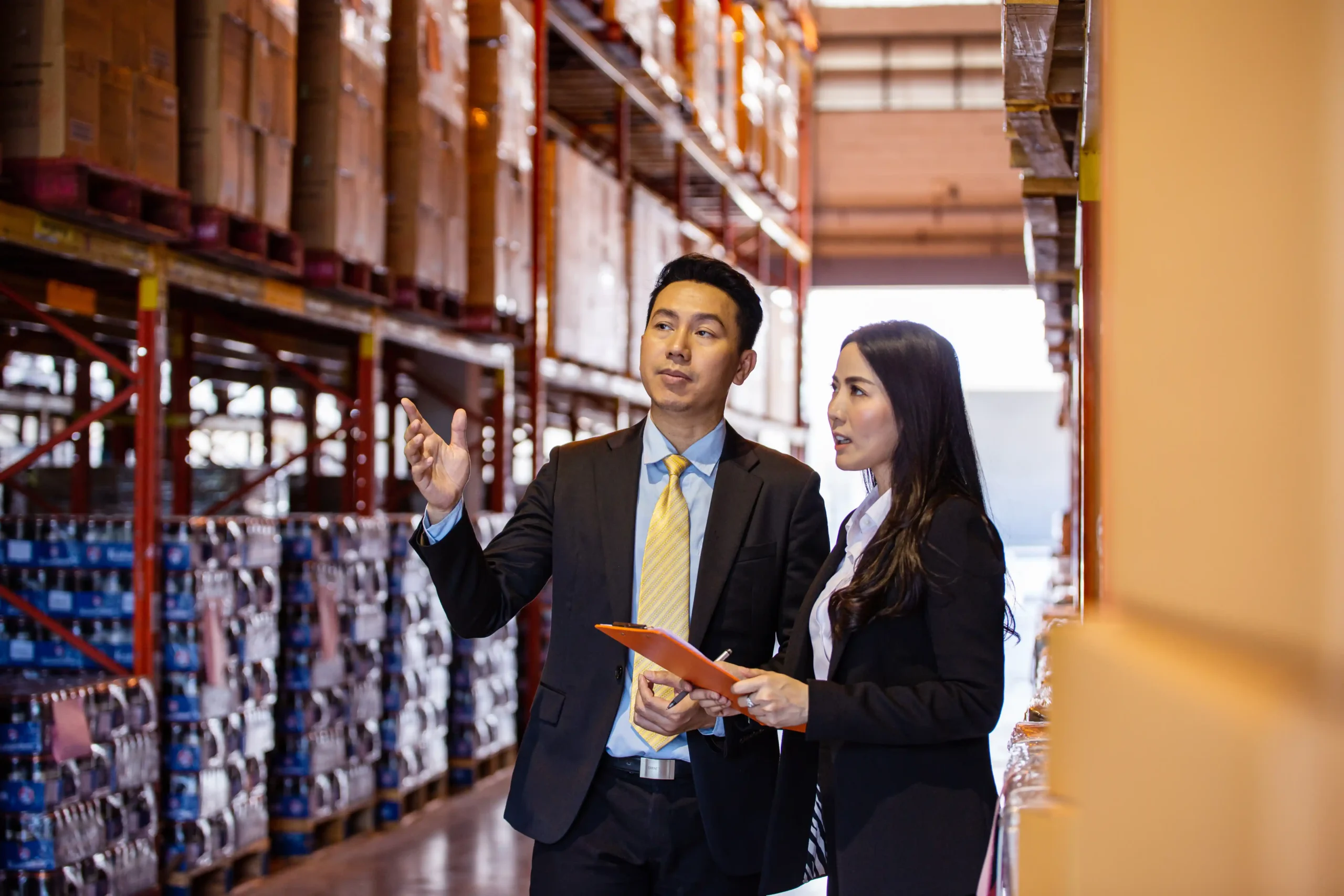 Two business professionals inspecting inventory racks inside a small commercial warehouse for rent during a walkthrough.
