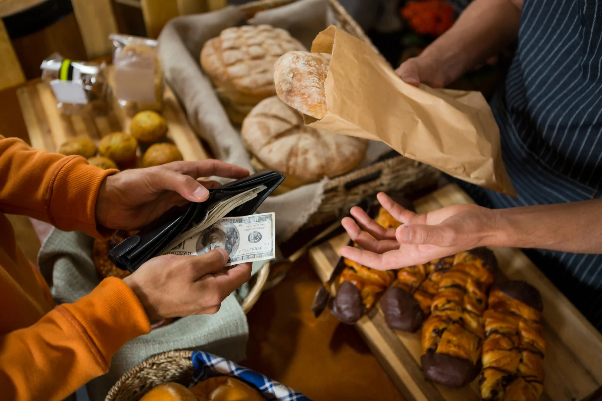 A customer paying cash at a bakery counter, symbolizing rising consumer costs and pricing changes caused by de minimis end 2025.