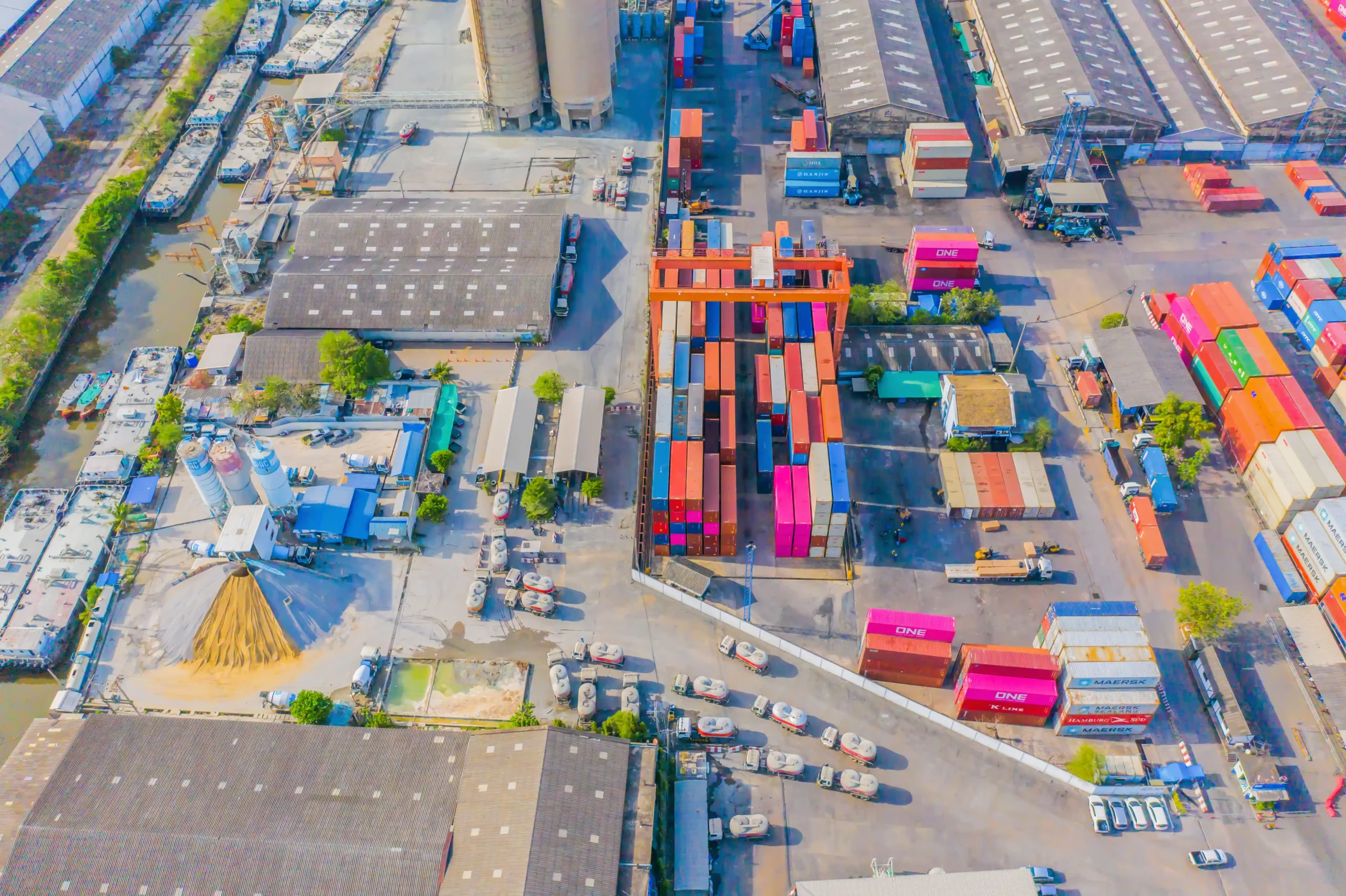 Aerial view of a busy logistics port with shipping containers and cargo trucks, showing how U.S. supply chains are adjusting to the new import duty rules for $800 shipments.