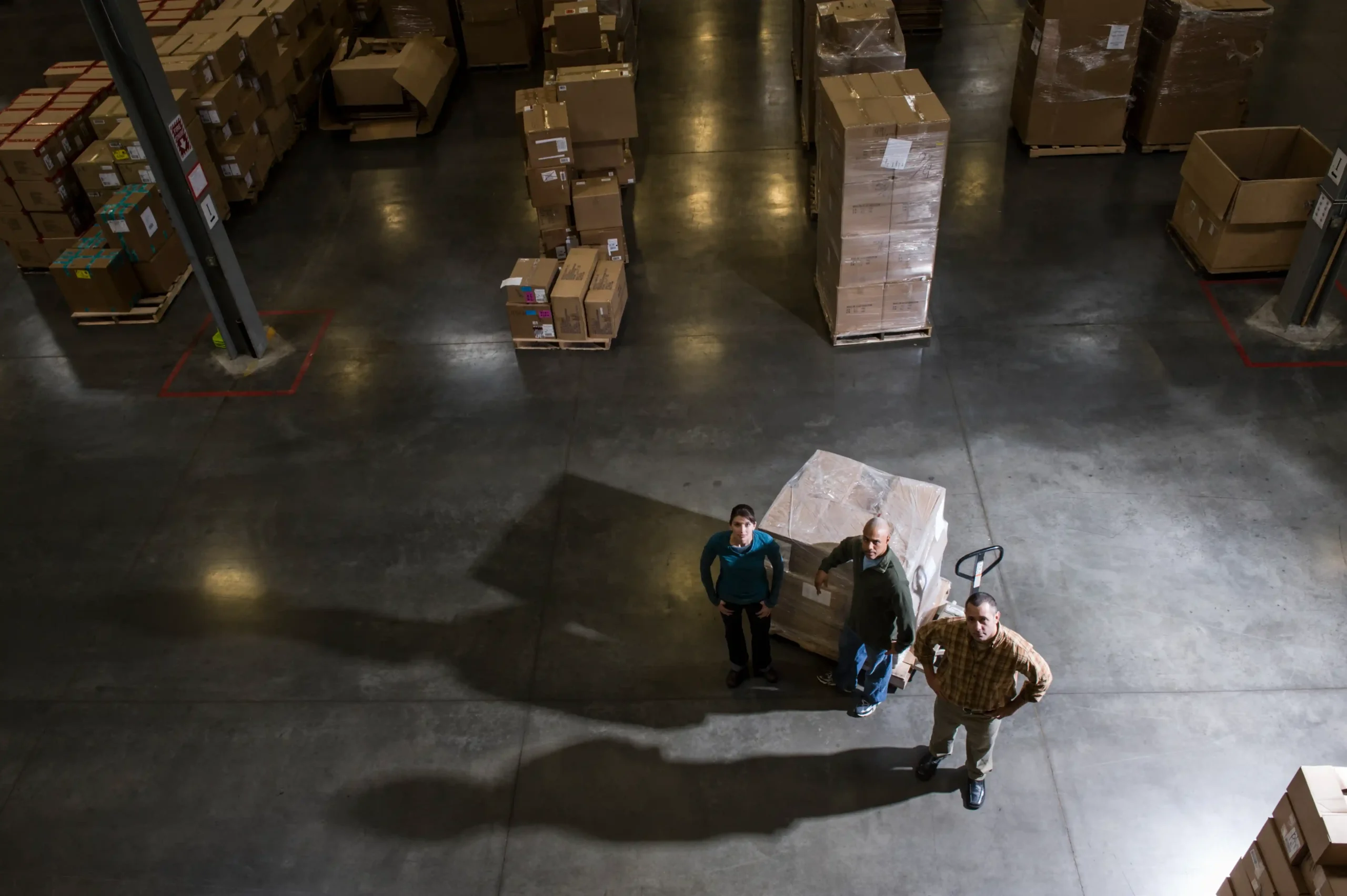 A warehouse team standing beside palletized goods in a large distribution center, illustrating pre-automation workflows before adopting an automated warehouse storage system.