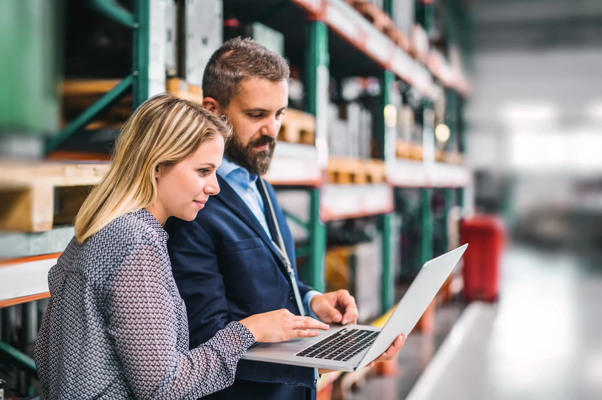 Business professionals reviewing warehouse data on a laptop while using warehouse storage management software in an organized facility.