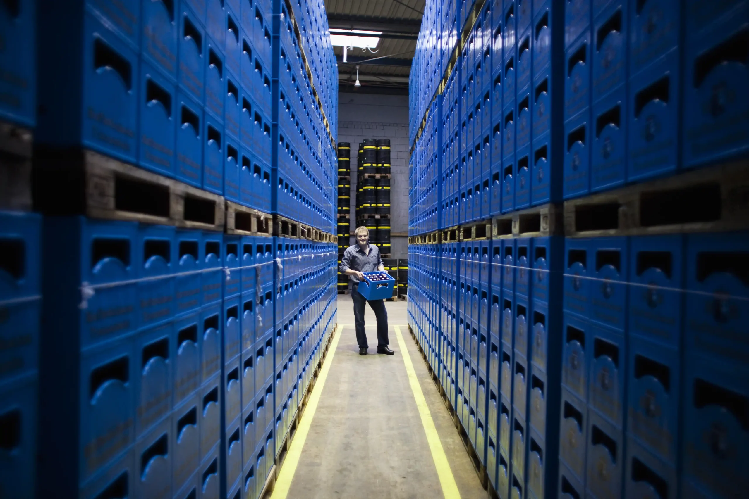 Worker carrying crates between tall warehouse racks, representing how organized data warehouse storage improves visibility and operational flow.