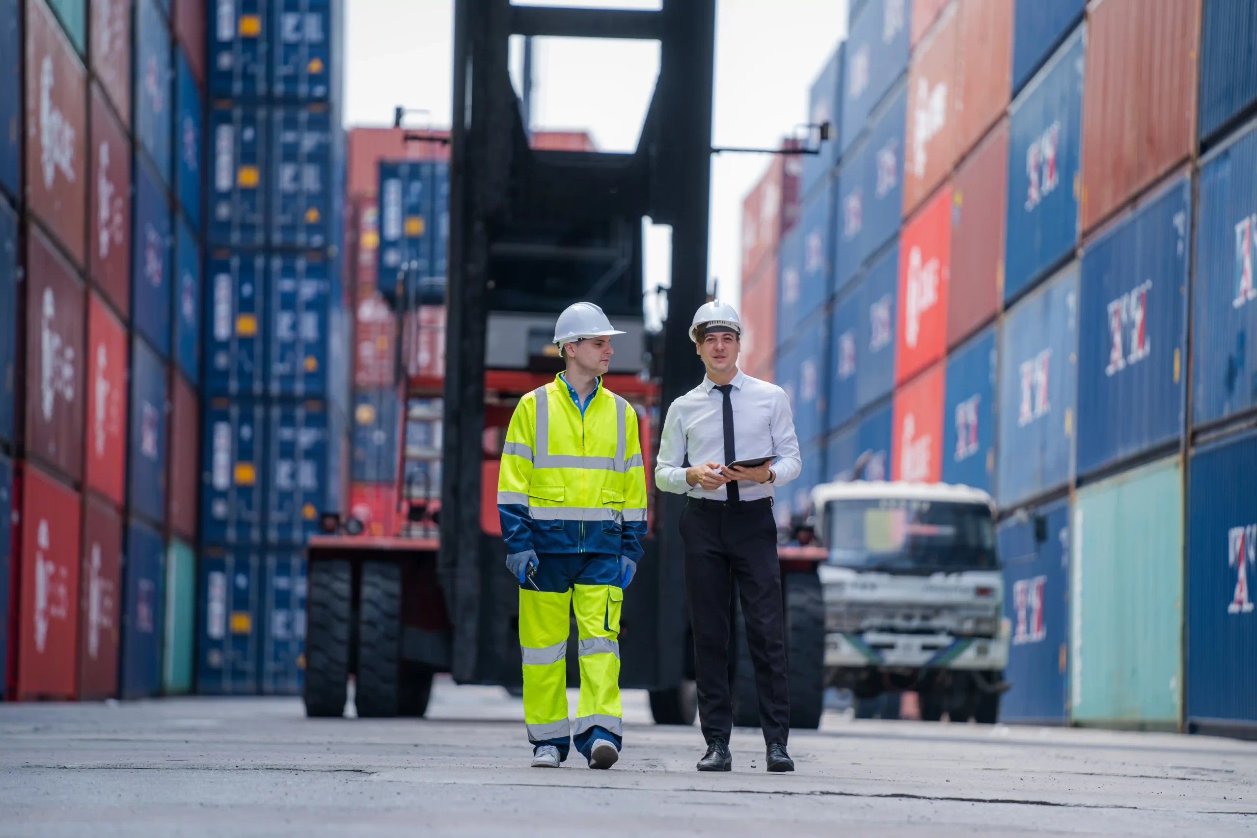 Logistics manager and warehouse worker walking through container stacks during global warehouse and logistics planning