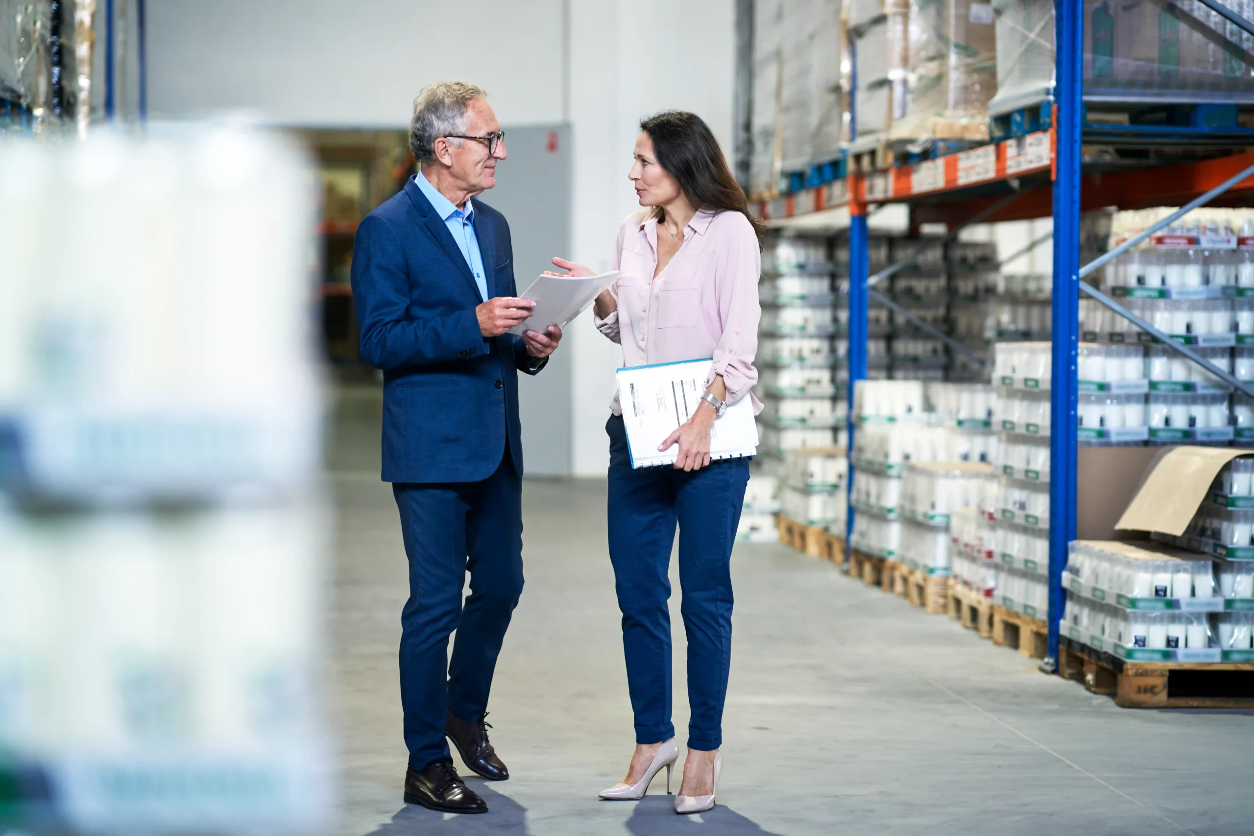 Two warehouse managers discussing documents in a storage facility, illustrating the importance of warehouse storage insurance for protecting inventory.