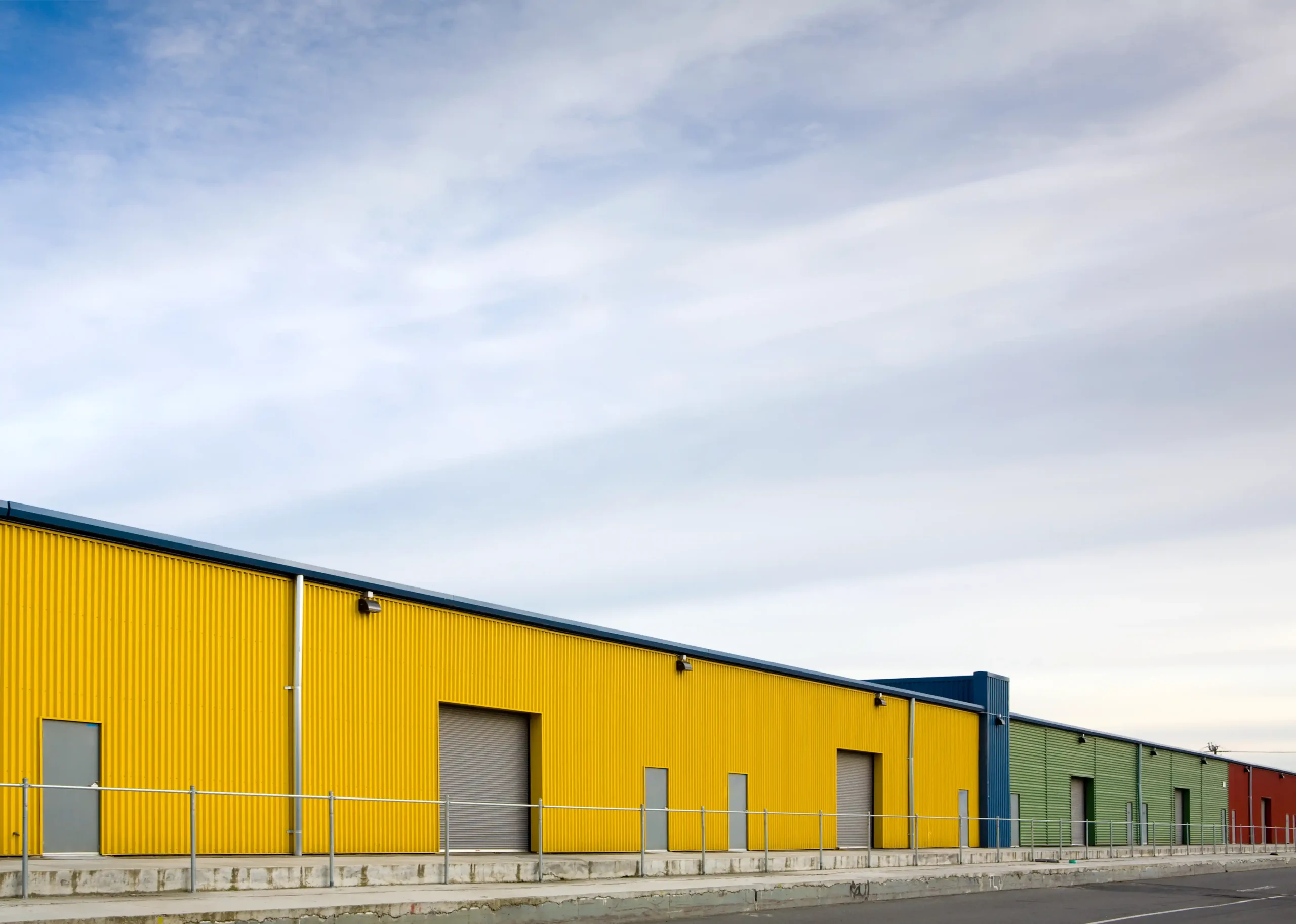 Bright yellow and green warehouse storage building with roll-up doors in an industrial area used for commercial storage operations.